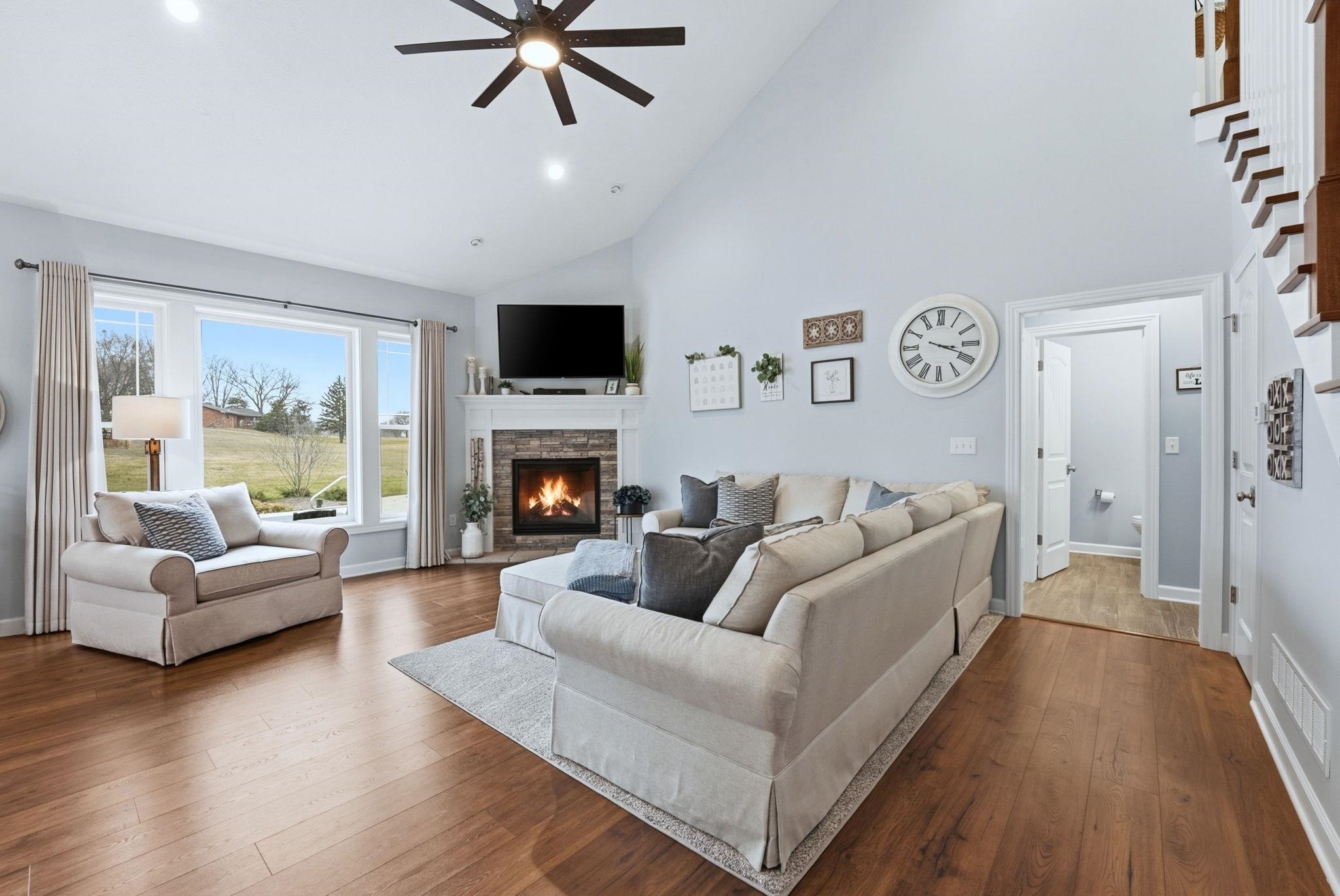 Living area featuring ceiling fan, dark wood finished floors, a stone fireplace, lofted ceiling, and recessed lighting