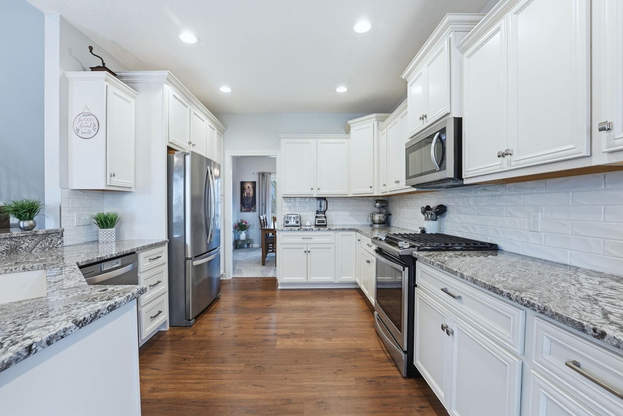 Kitchen featuring light stone counters, stainless steel appliances, white cabinetry, dark wood-type flooring, and recessed lighting