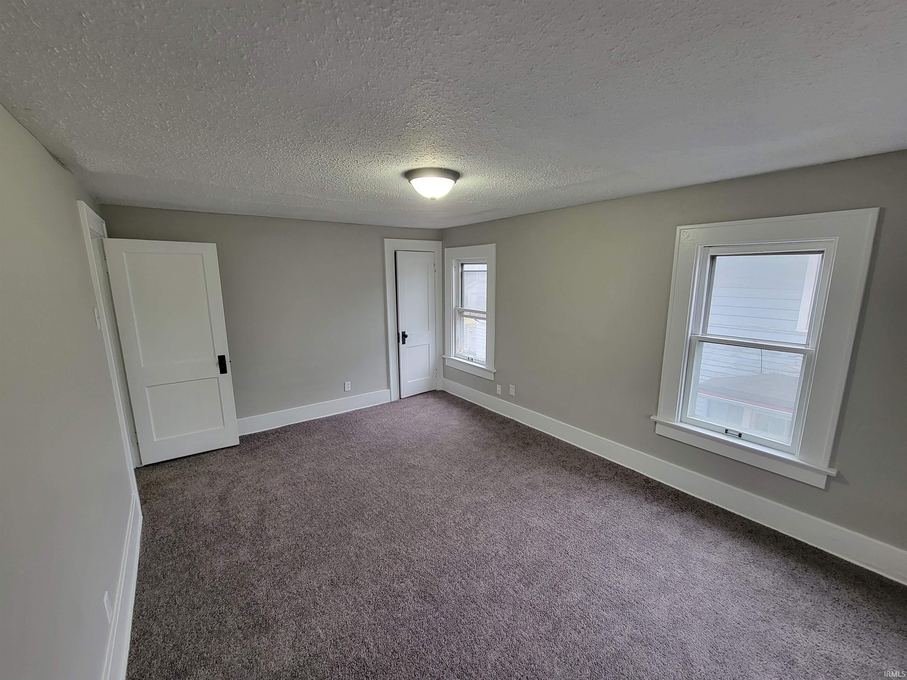 Unfurnished room featuring a textured ceiling and dark carpet