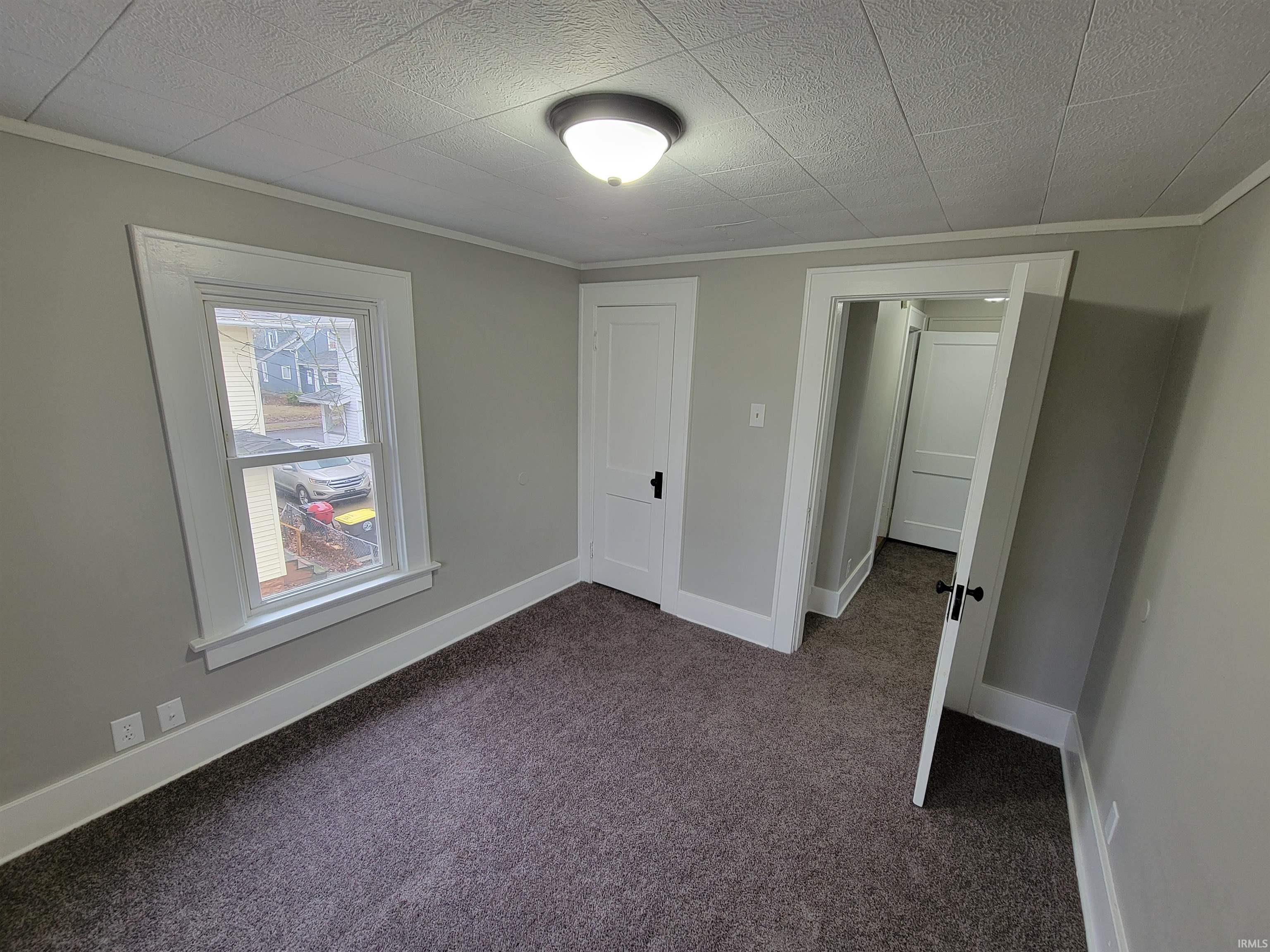 Unfurnished bedroom with dark carpet and crown molding