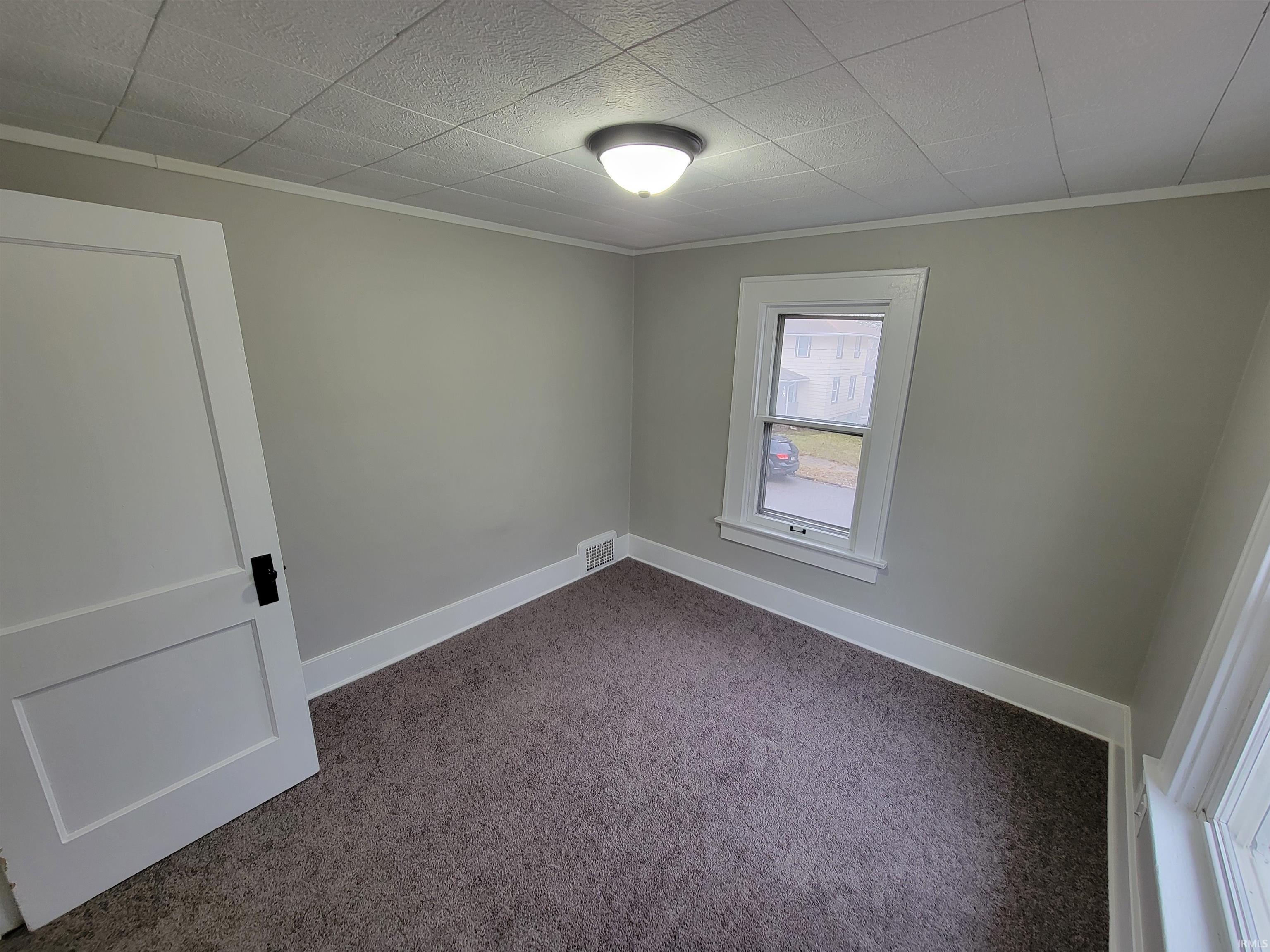 Unfurnished room featuring dark colored carpet and crown molding