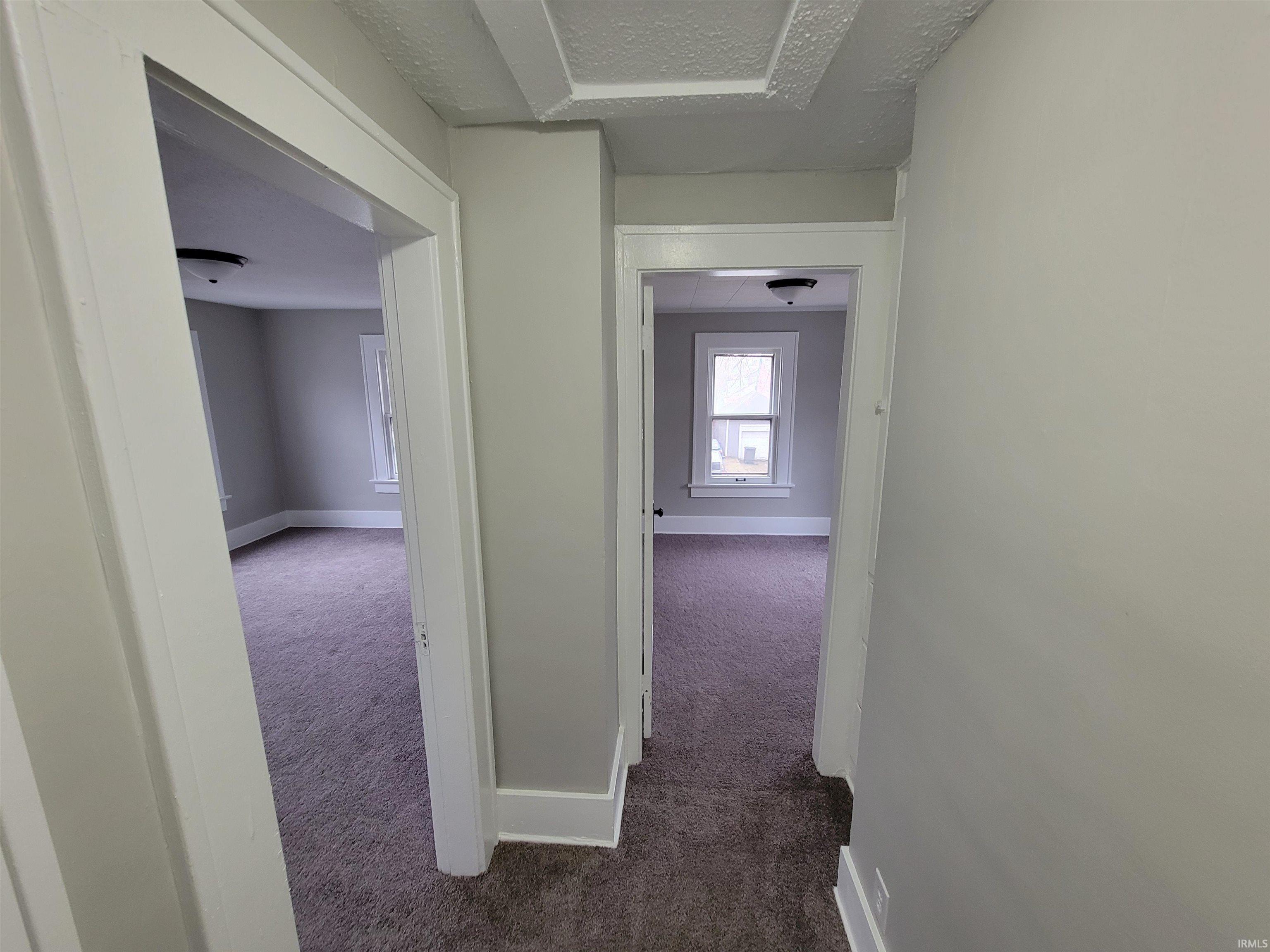 Corridor featuring a textured ceiling and dark colored carpet