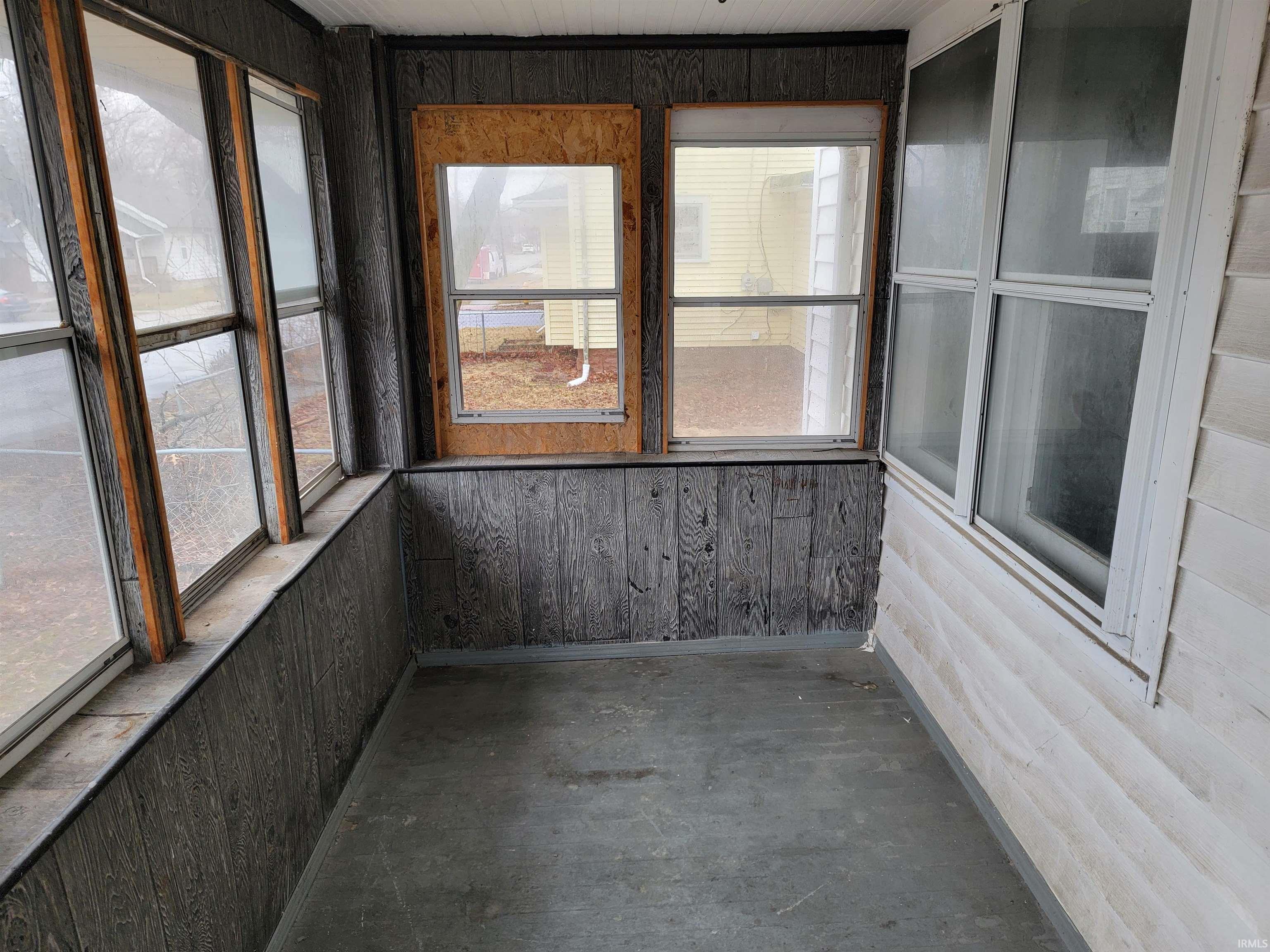 Unfurnished sunroom featuring wooden walls and unfinished concrete flooring