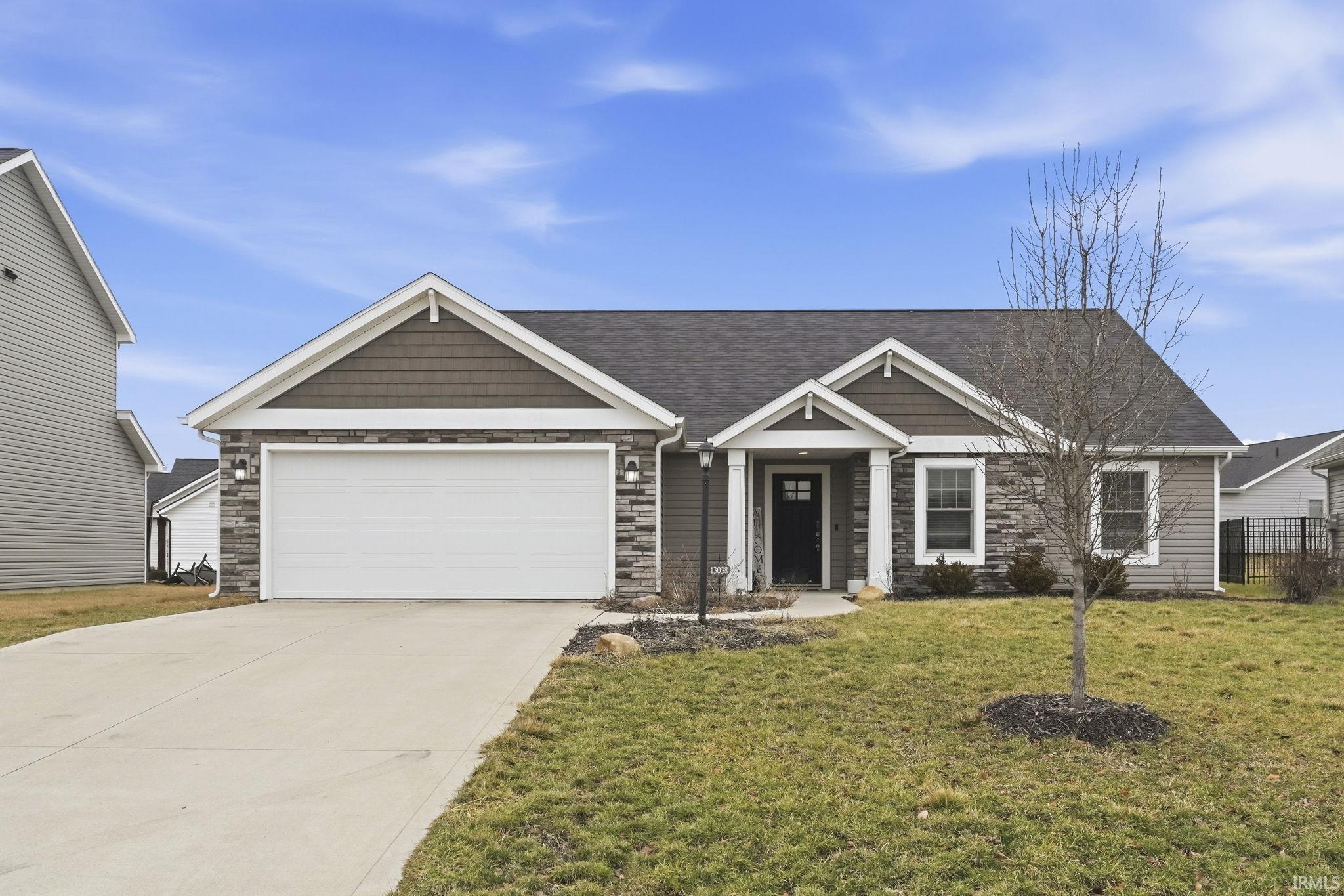 Craftsman-style house with driveway, stone siding, an attached garage, a front yard, and a shingled roof