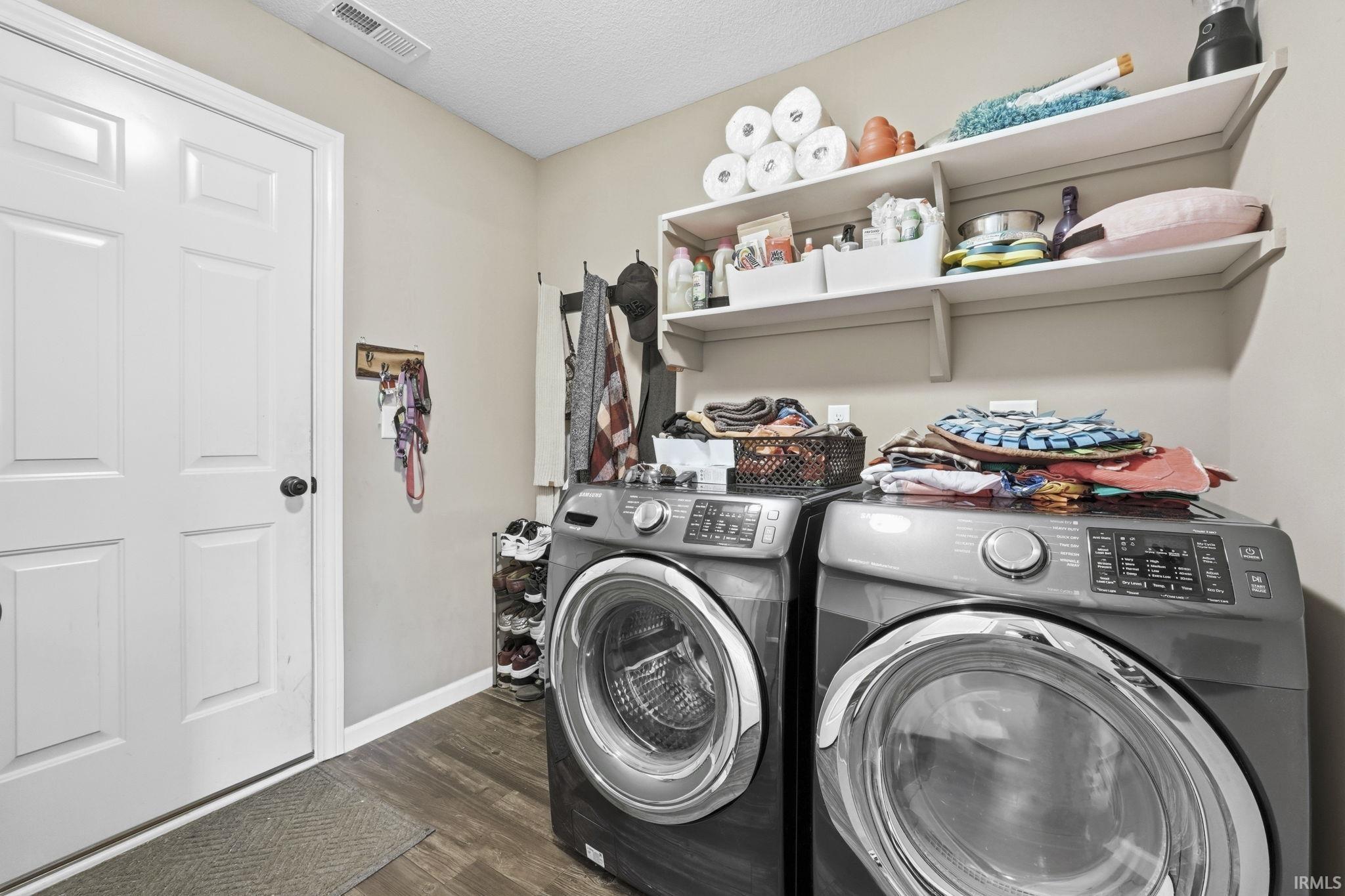 Laundry room with washing machine and clothes dryer, dark wood finished floors, and a textured ceiling
