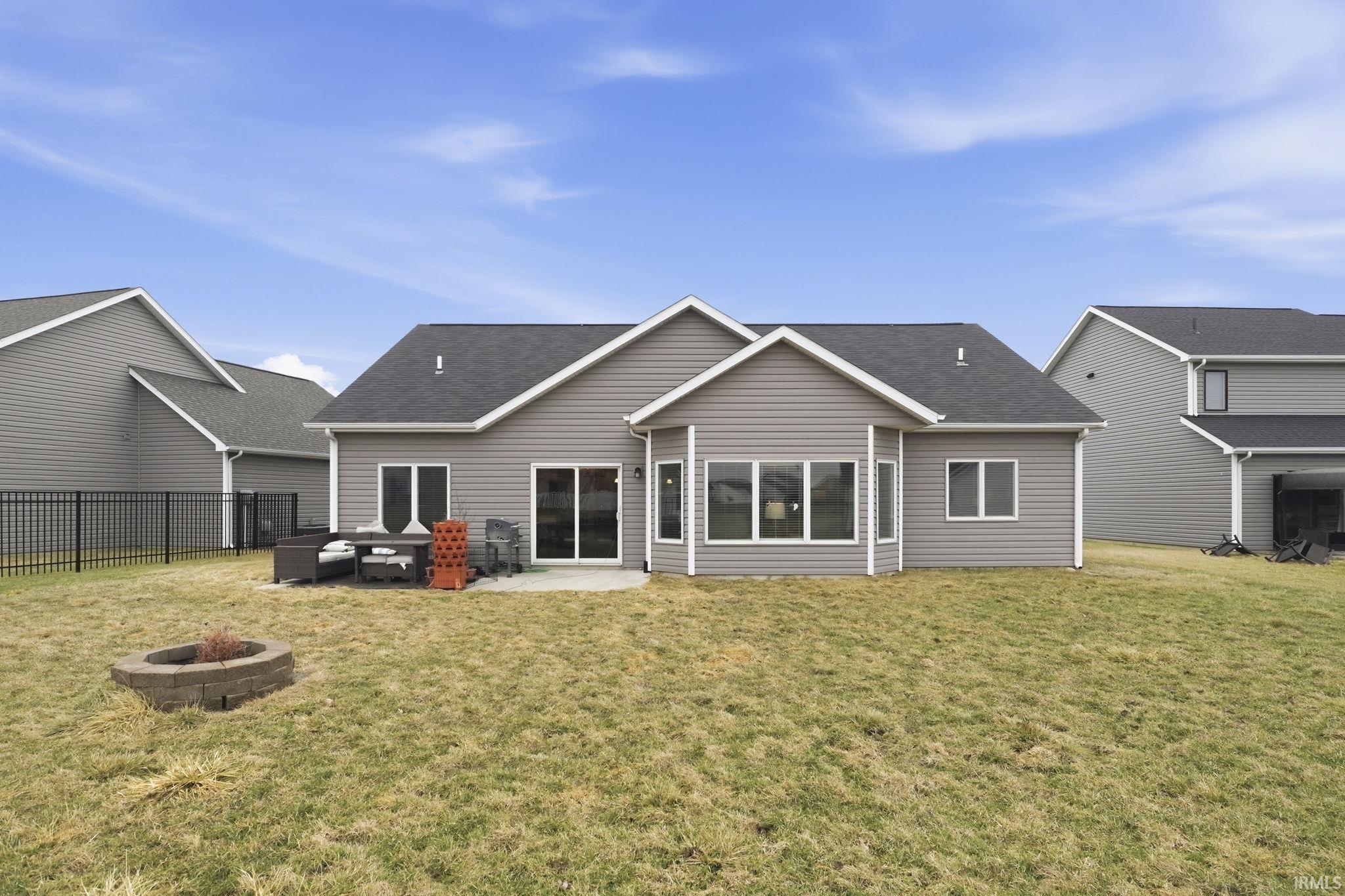 Rear view of house featuring roof with shingles, a patio area, a lawn, and an outdoor fire pit
