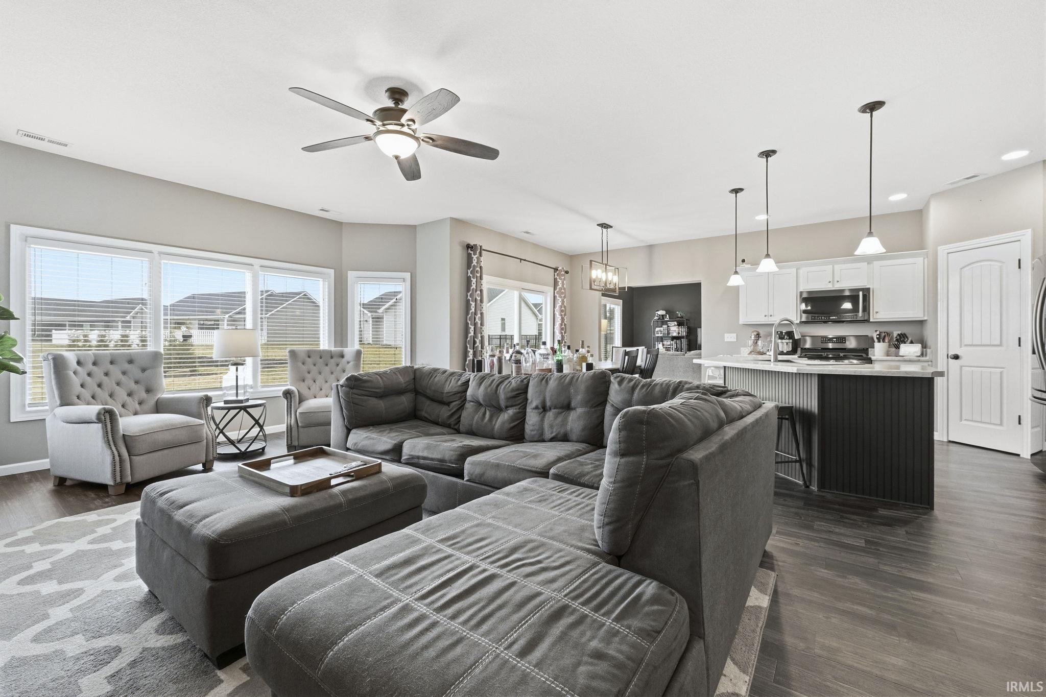 Living area with dark wood-style flooring, ceiling fan, and a chandelier