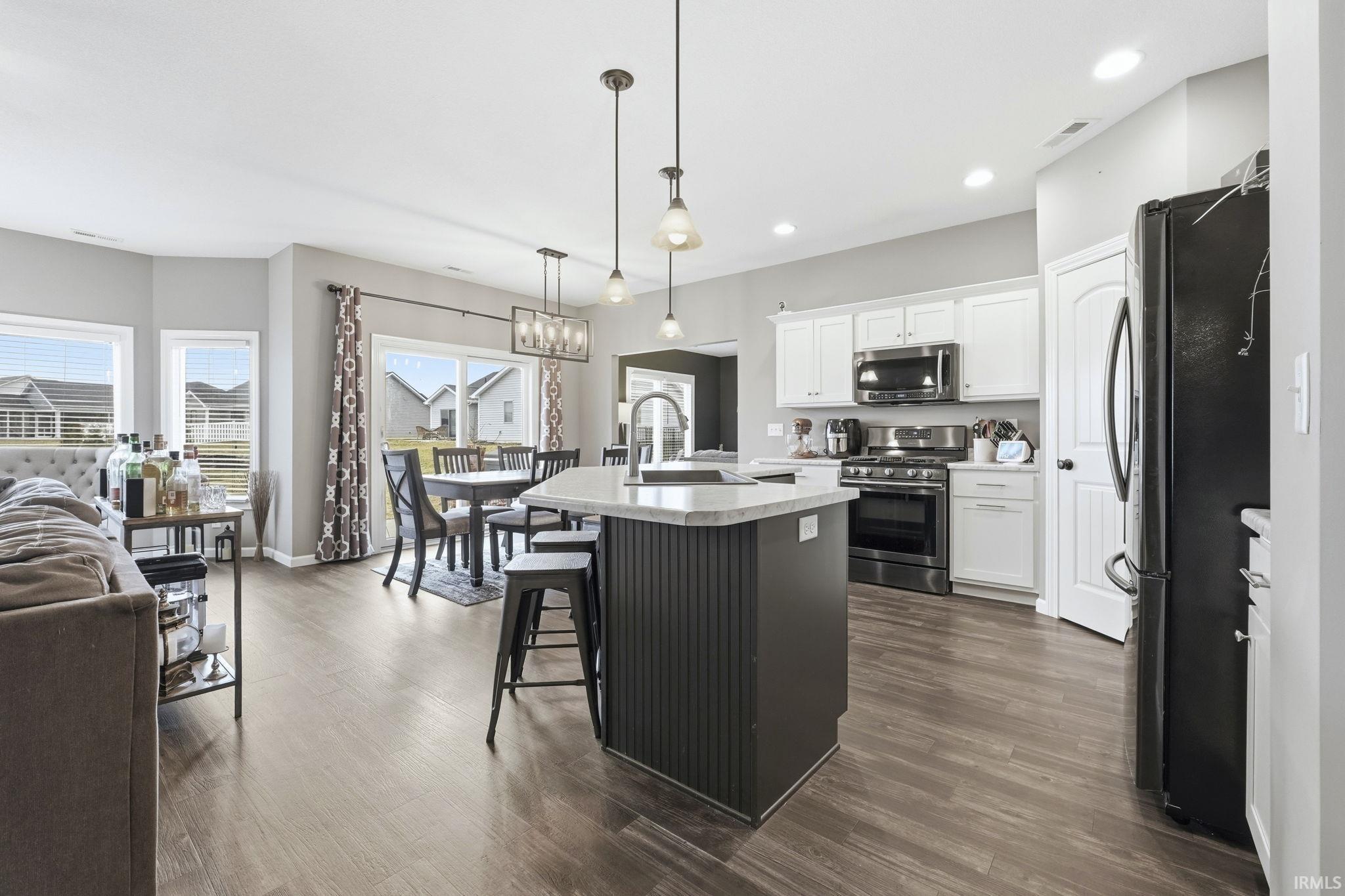 Two tone kitchen featuring stainless steel appliances, a center island with sink, decorative light fixtures, a breakfast bar, and dark wood-style flooring