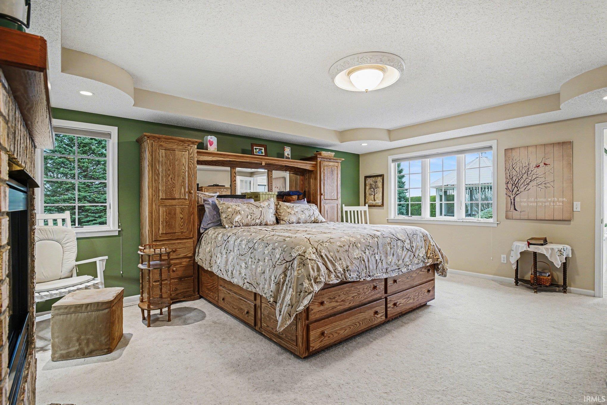 Bedroom with multiple windows, light carpet, a tray ceiling, a large fireplace, and recessed lighting