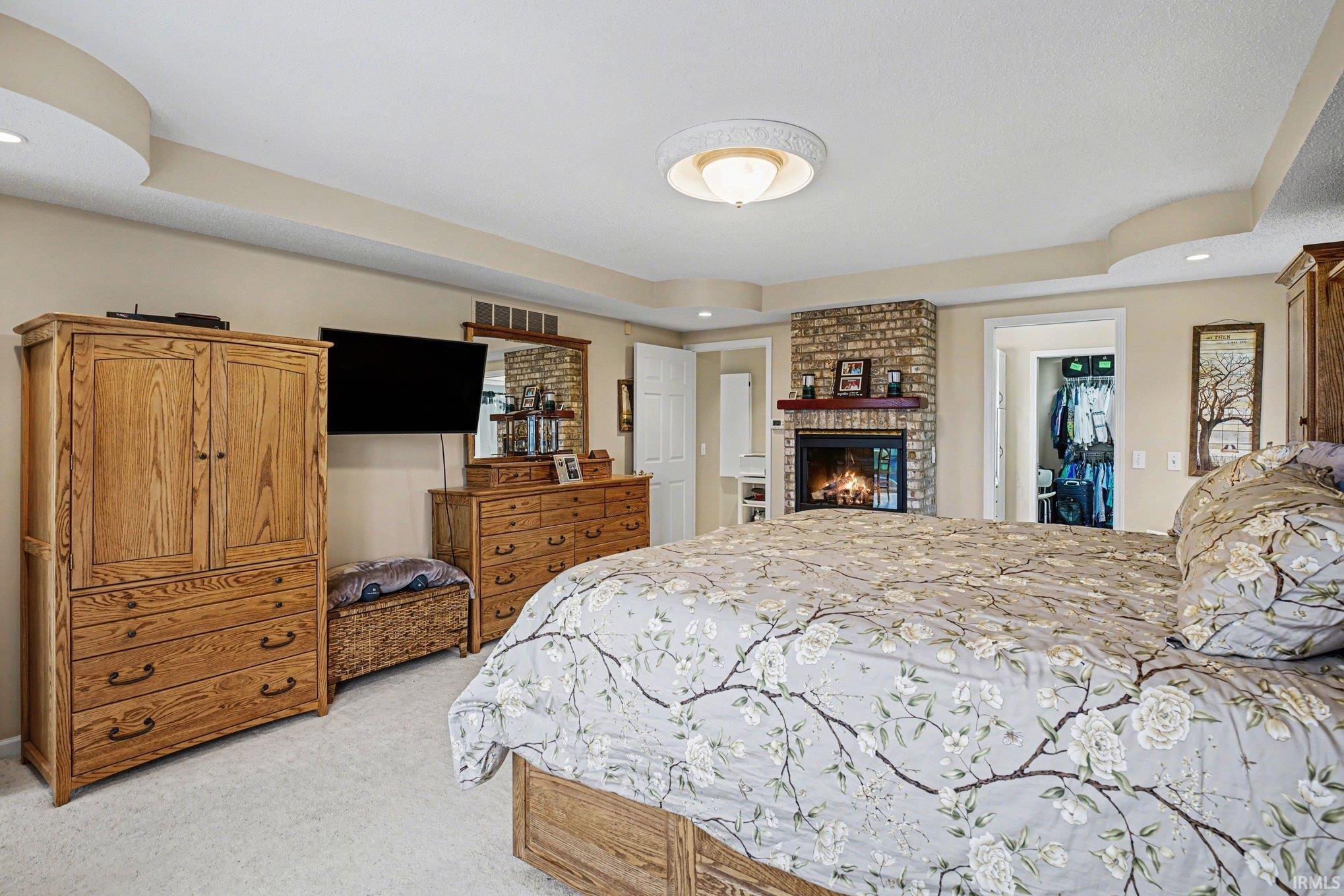 Bedroom featuring recessed lighting, a fireplace, light carpet, and a raised ceiling