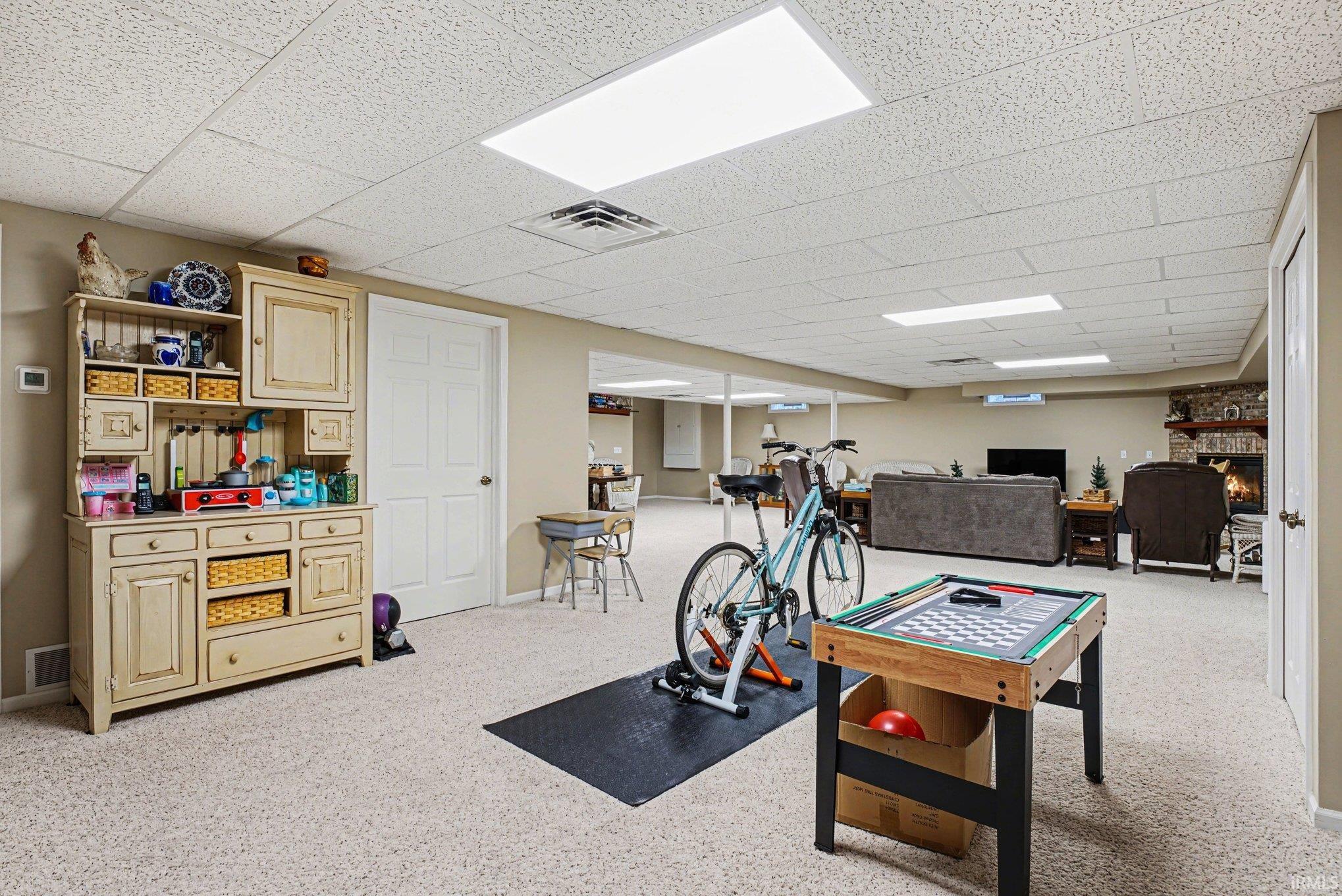 Playroom featuring a drop ceiling, a large fireplace, and light colored carpet