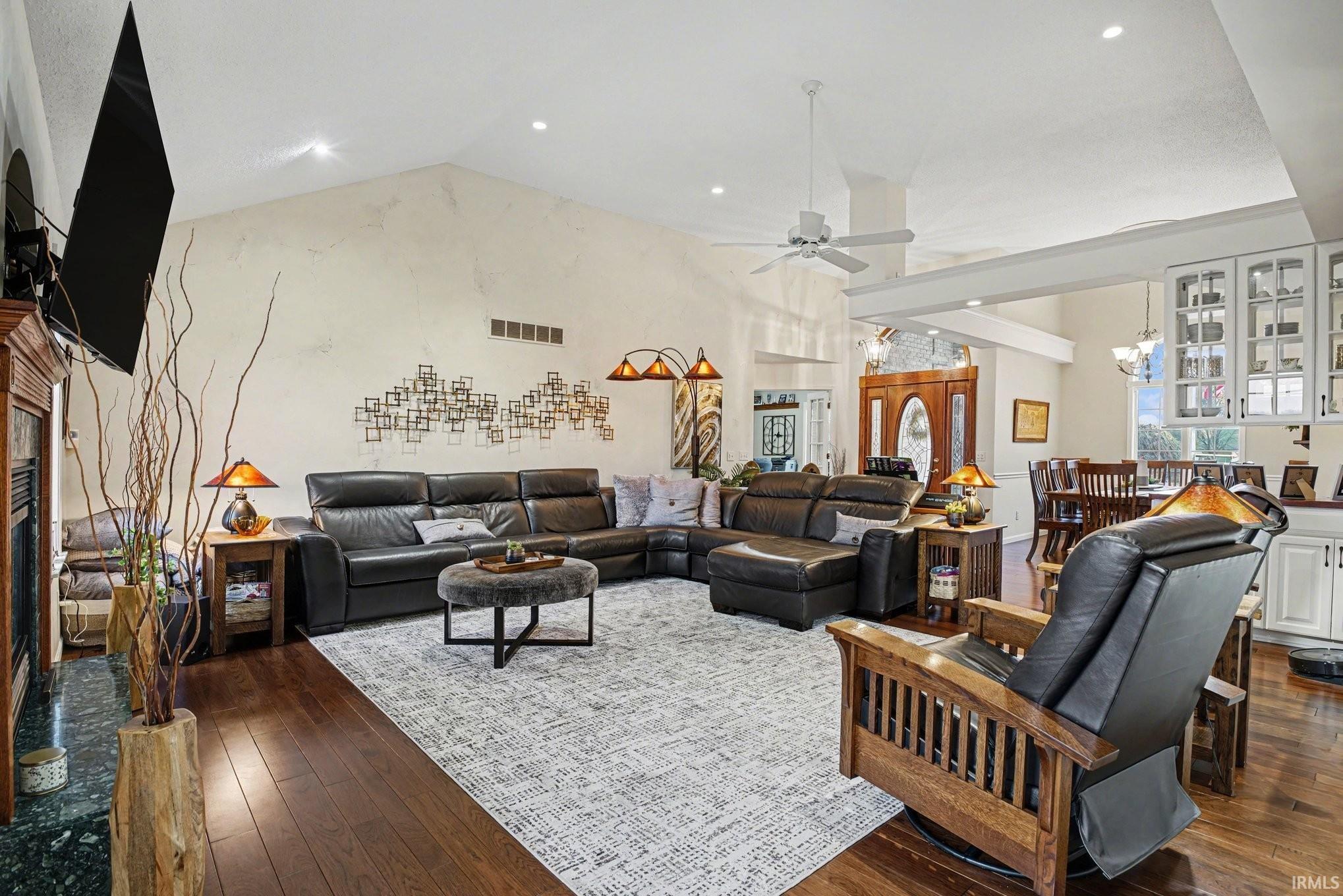Living room featuring a fireplace, dark wood-style flooring, ceiling fan, hanging lights, and a high ceiling
