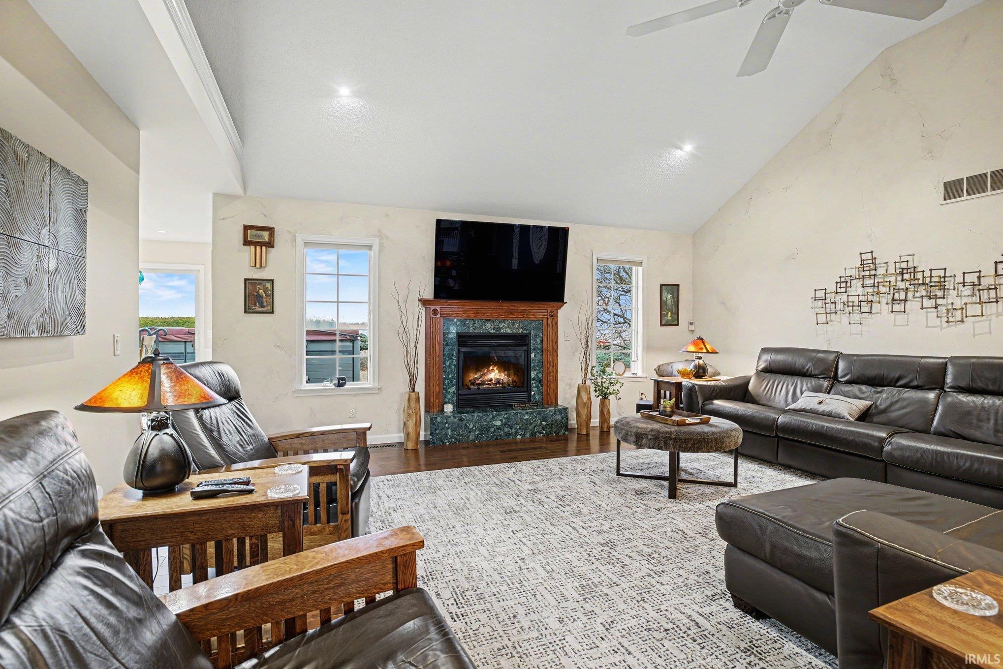 Living room with wood finished floors, a fireplace, healthy amount of natural light, vaulted ceiling, and ceiling fan