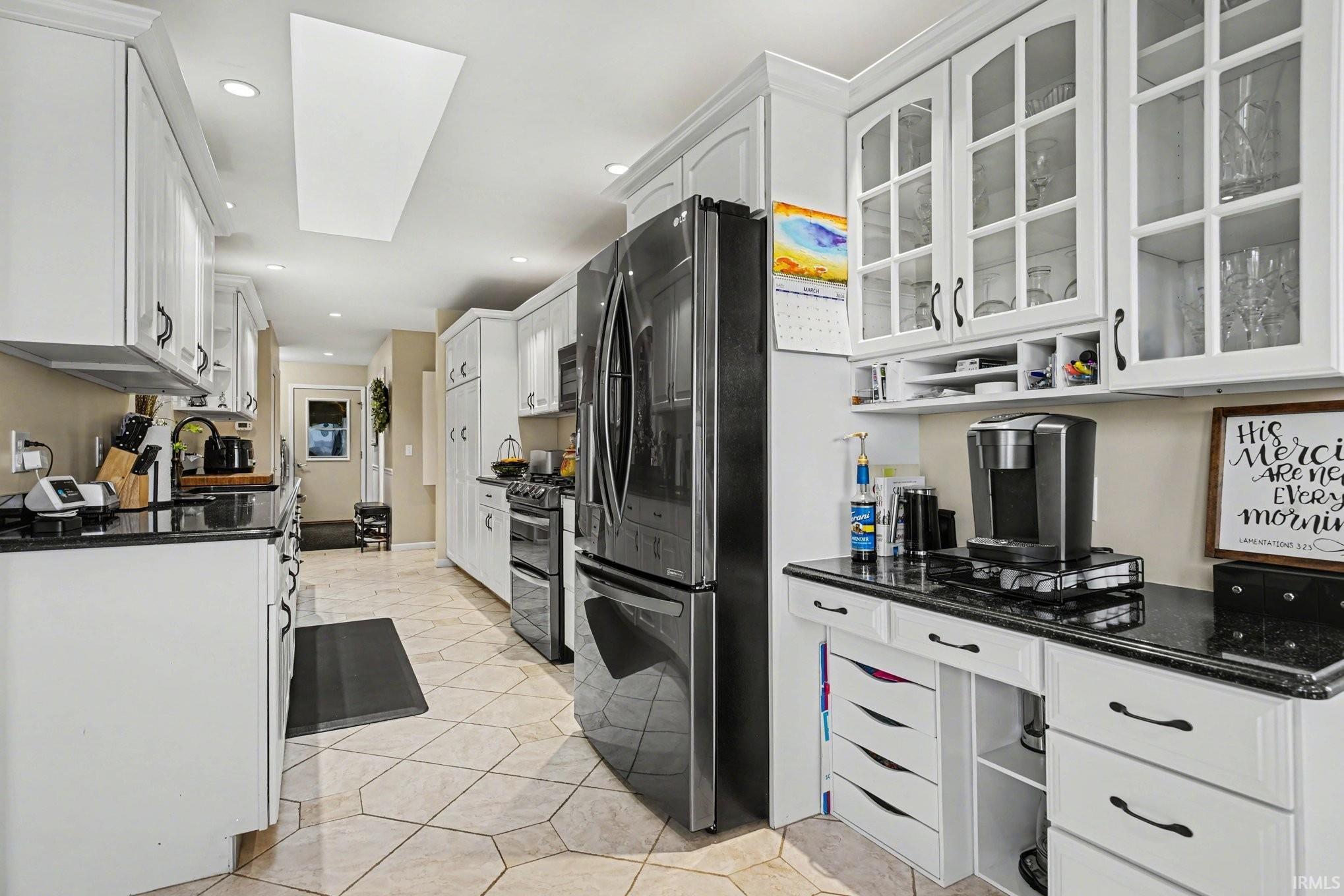 Kitchen featuring white cabinetry, refrigerator with ice dispenser, dark stone countertops, glass fronted cabinets, and light tile patterned floors