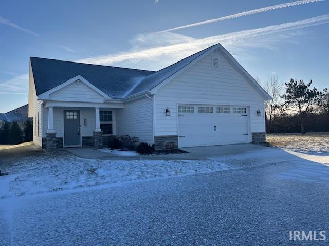 View of front of house with covered porch, driveway, a garage, and stone siding