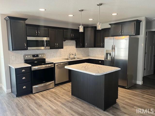 Kitchen with stainless steel appliances, a center island, dark cabinets, and light wood finished floors