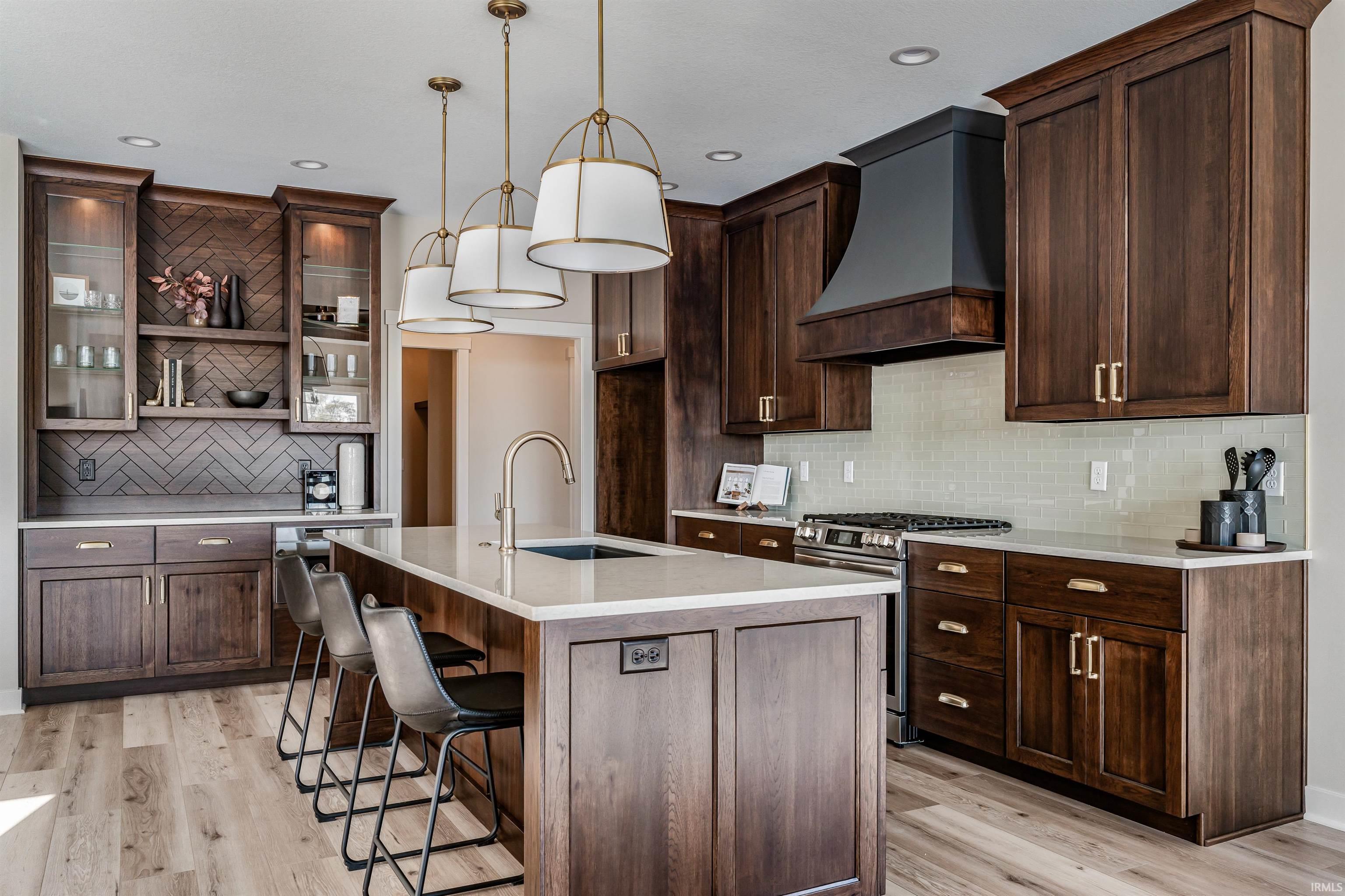 Kitchen featuring gas range, dark wood finish cabinetry, glass insert cabinets, a kitchen bar, and light wood-type flooring