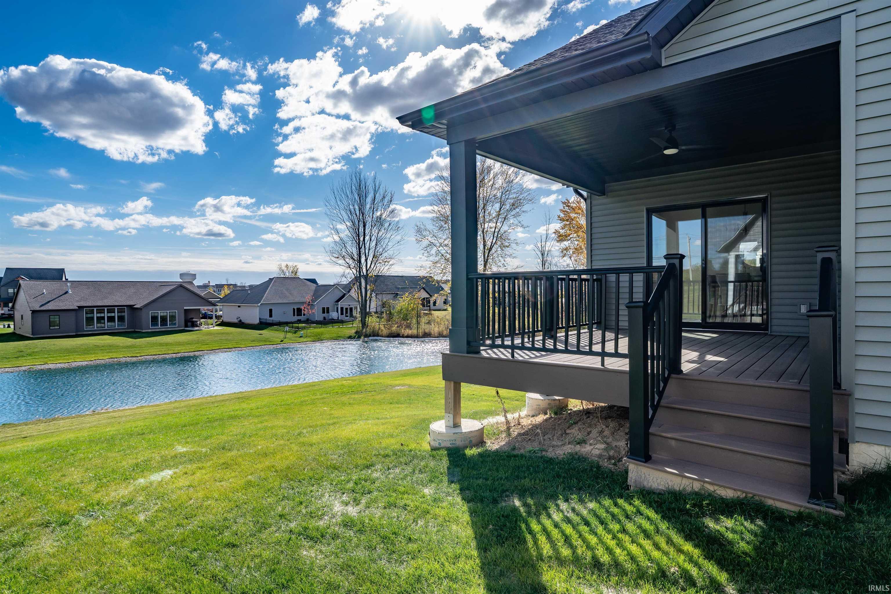 View of grassy yard featuring ceiling fan, a residential view, and a deck with water view