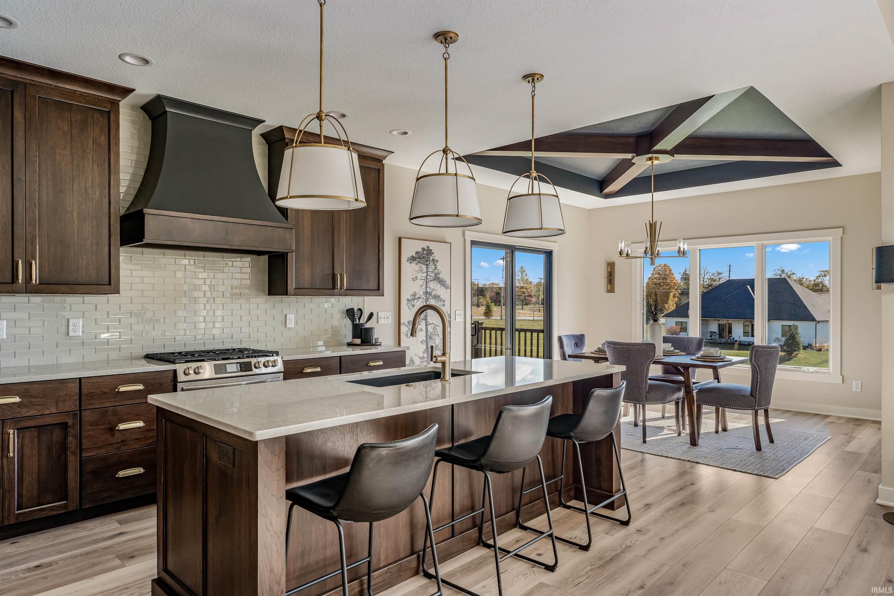 Kitchen with light stone counters, dark wood finish cabinetry, pendant lighting, a kitchen breakfast bar, and a kitchen island with sink