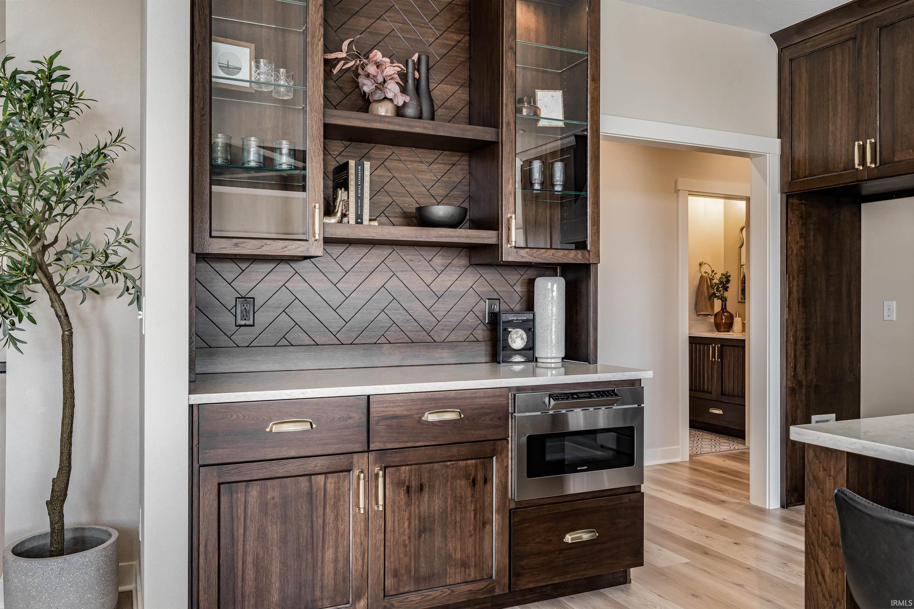 Kitchen featuring dark wood finish cabinetry, glass insert cabinets, open shelves, light wood-style flooring, and tasteful backsplash