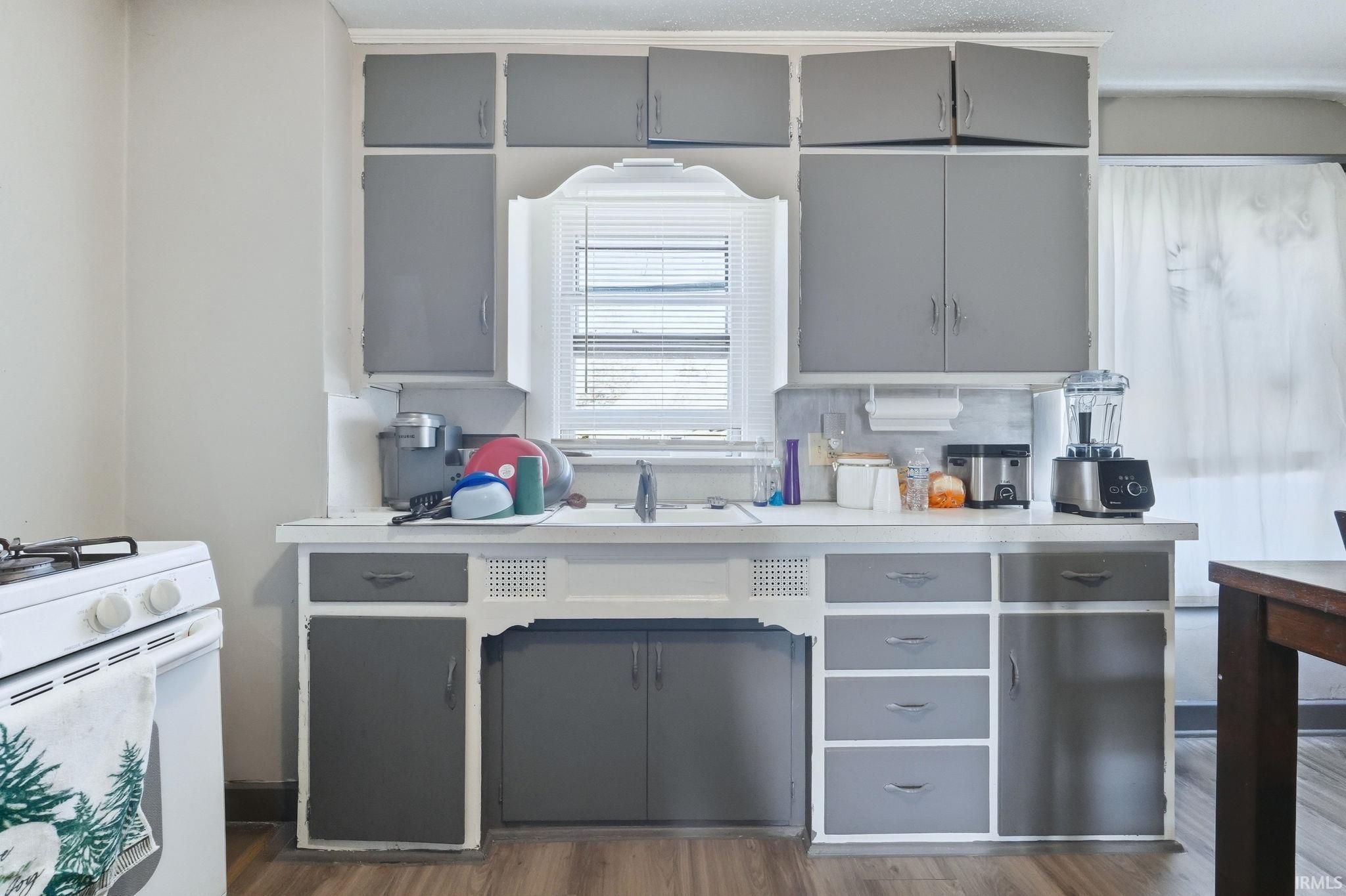 Two tone kitchen with light countertops, dark wood-type flooring, white range with gas stovetop, and two tone cabinets