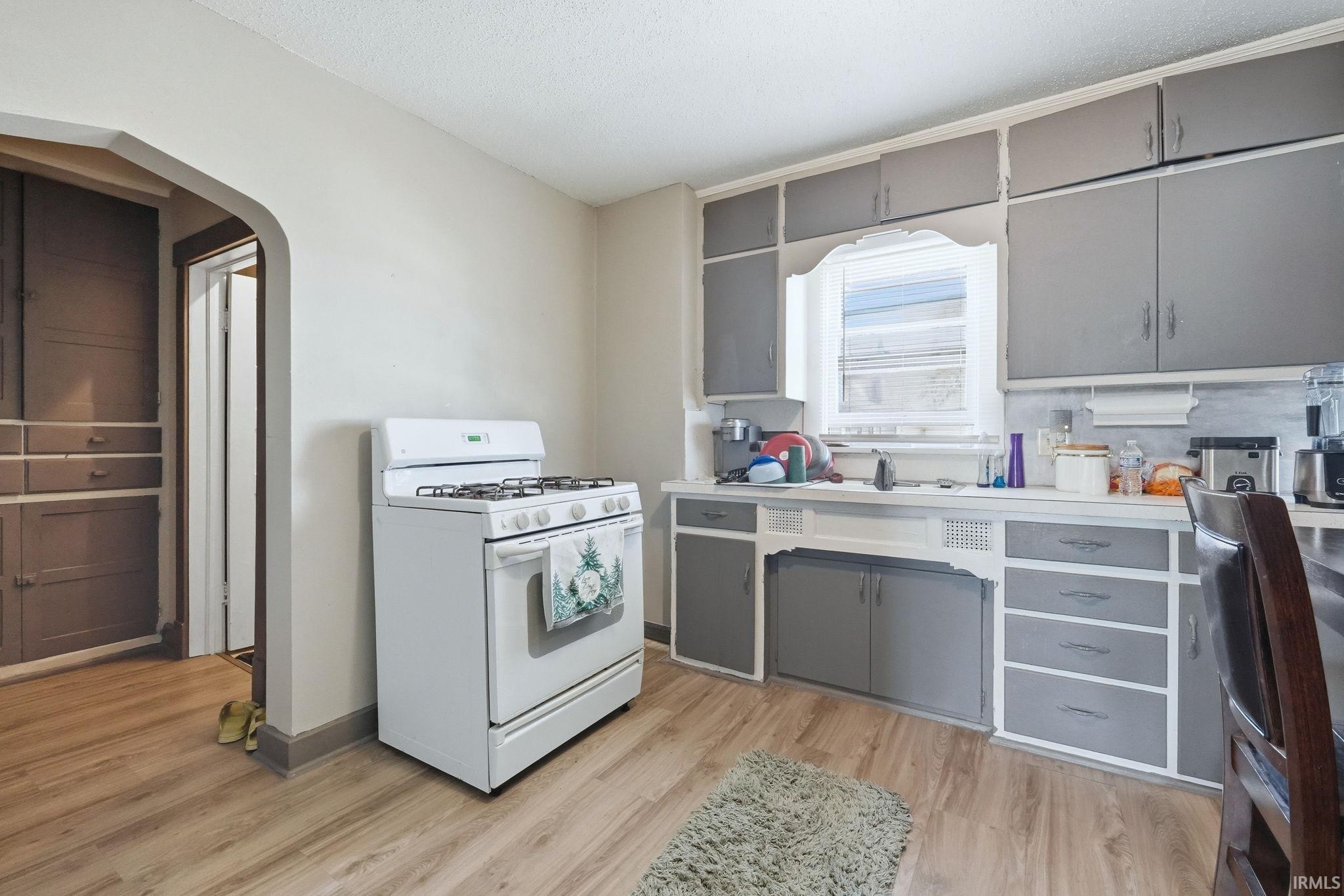 Kitchen with gray cabinetry, white range with gas stovetop, light countertops, arched walkways, and light wood-type flooring