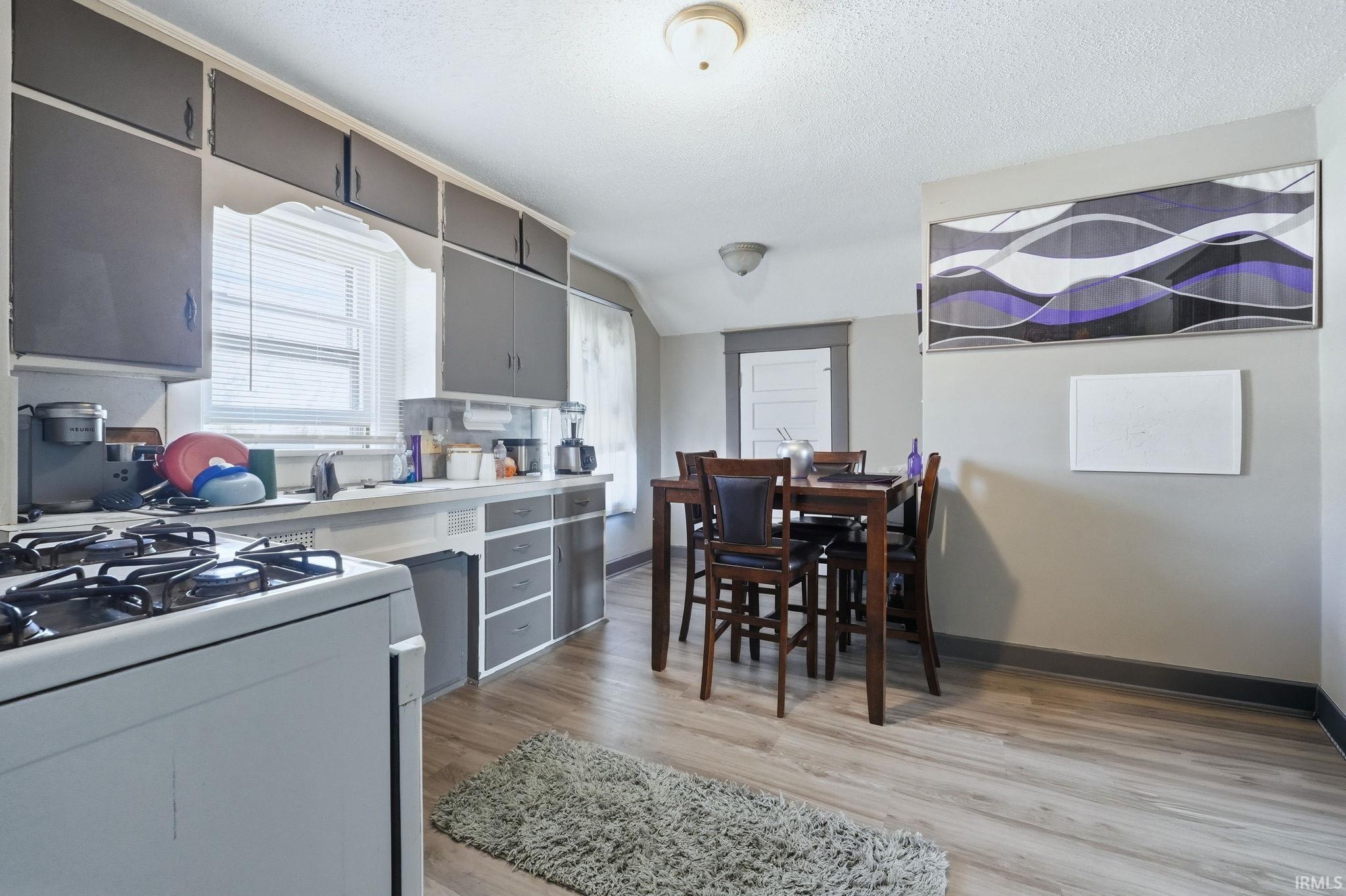 Kitchen featuring light countertops, white range with gas stovetop, light wood-style floors, gray cabinets, and a textured ceiling