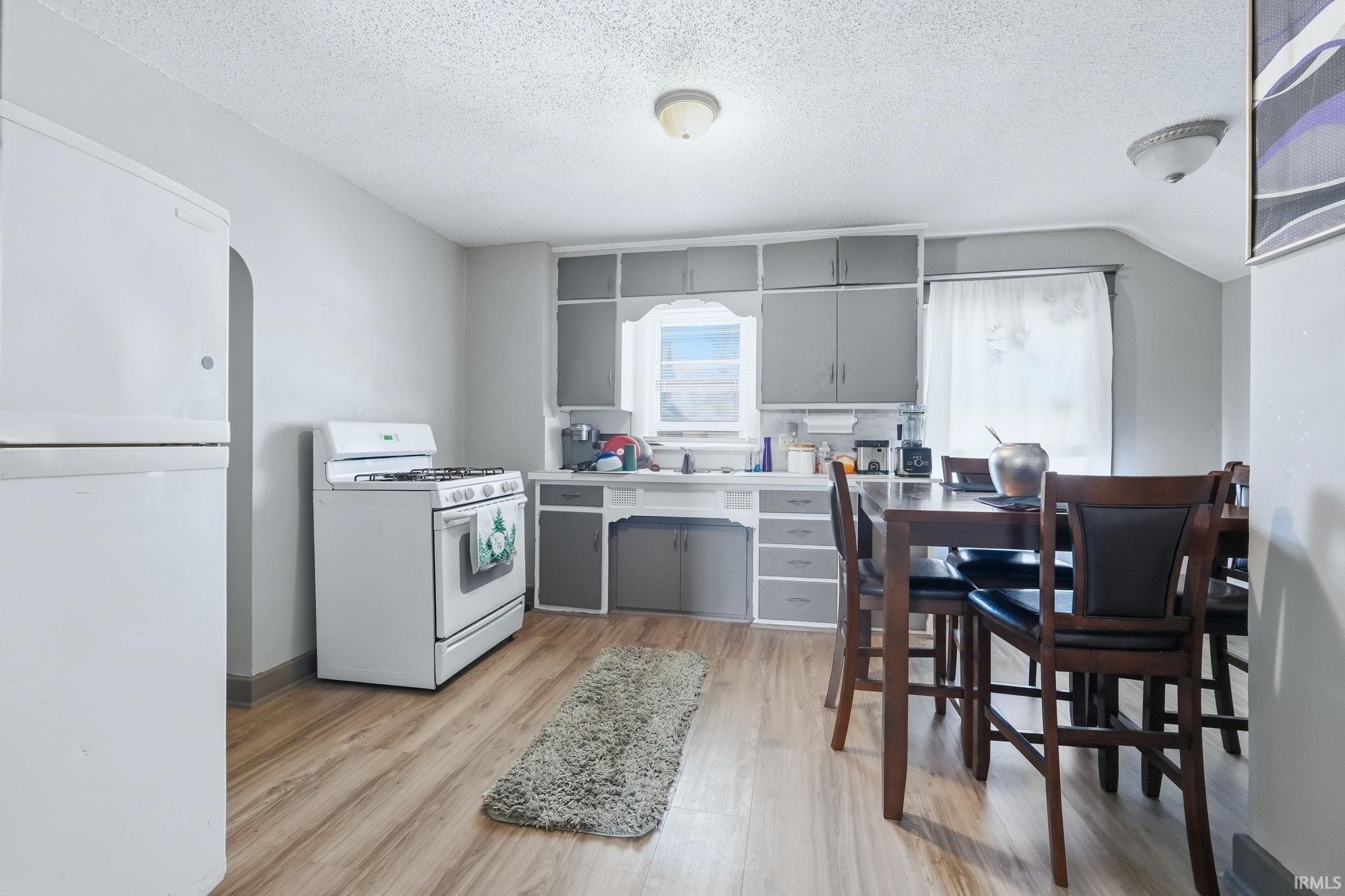 Kitchen featuring gray cabinets, white appliances, light countertops, light wood finished floors, and a textured ceiling