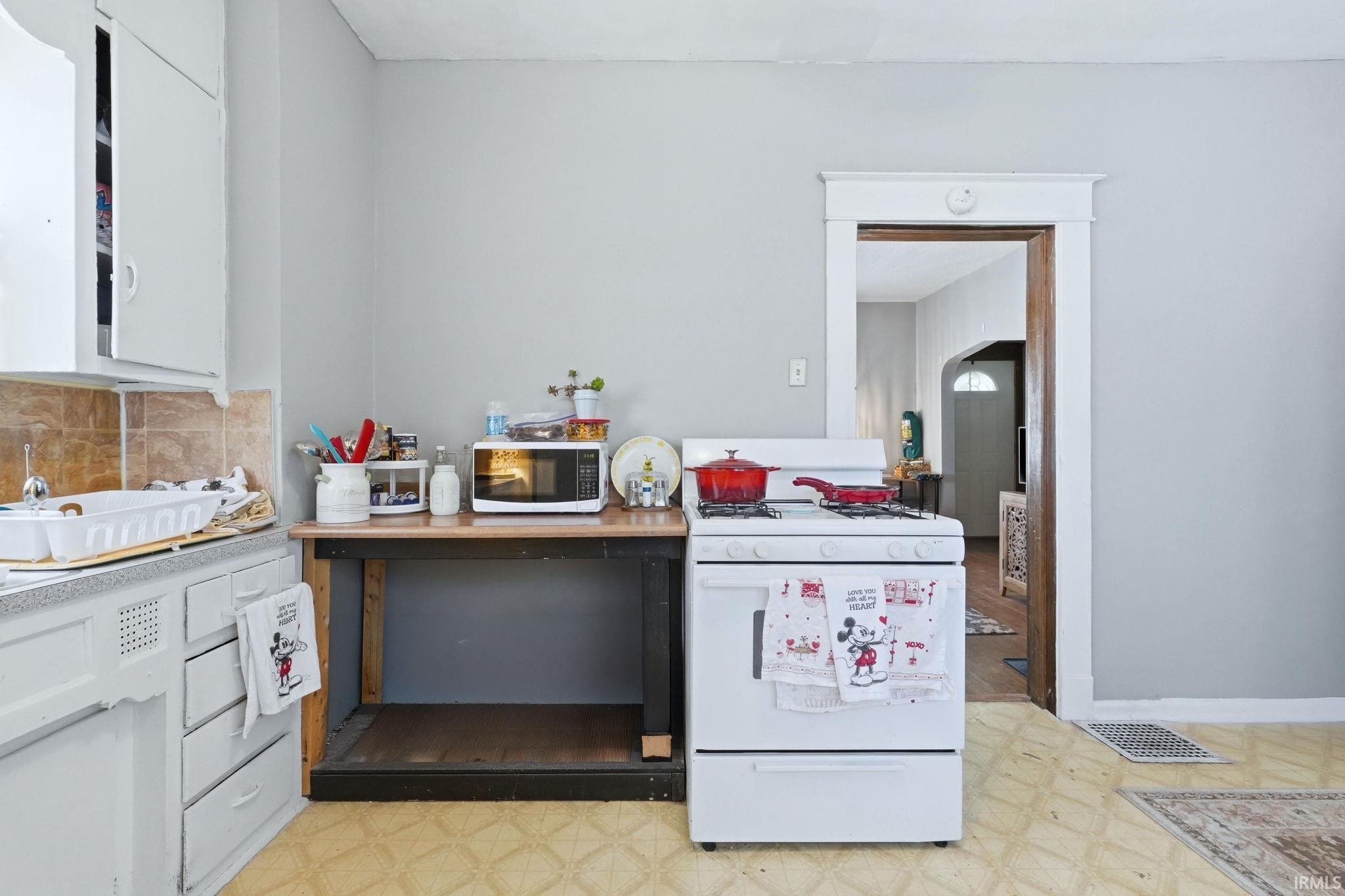 Kitchen featuring light floors, white appliances, white cabinetry, light countertops, and backsplash