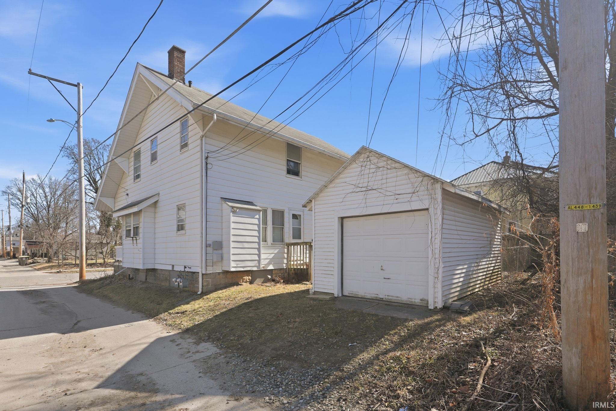 View of side of property with a garage, a chimney, driveway, and an outdoor structure