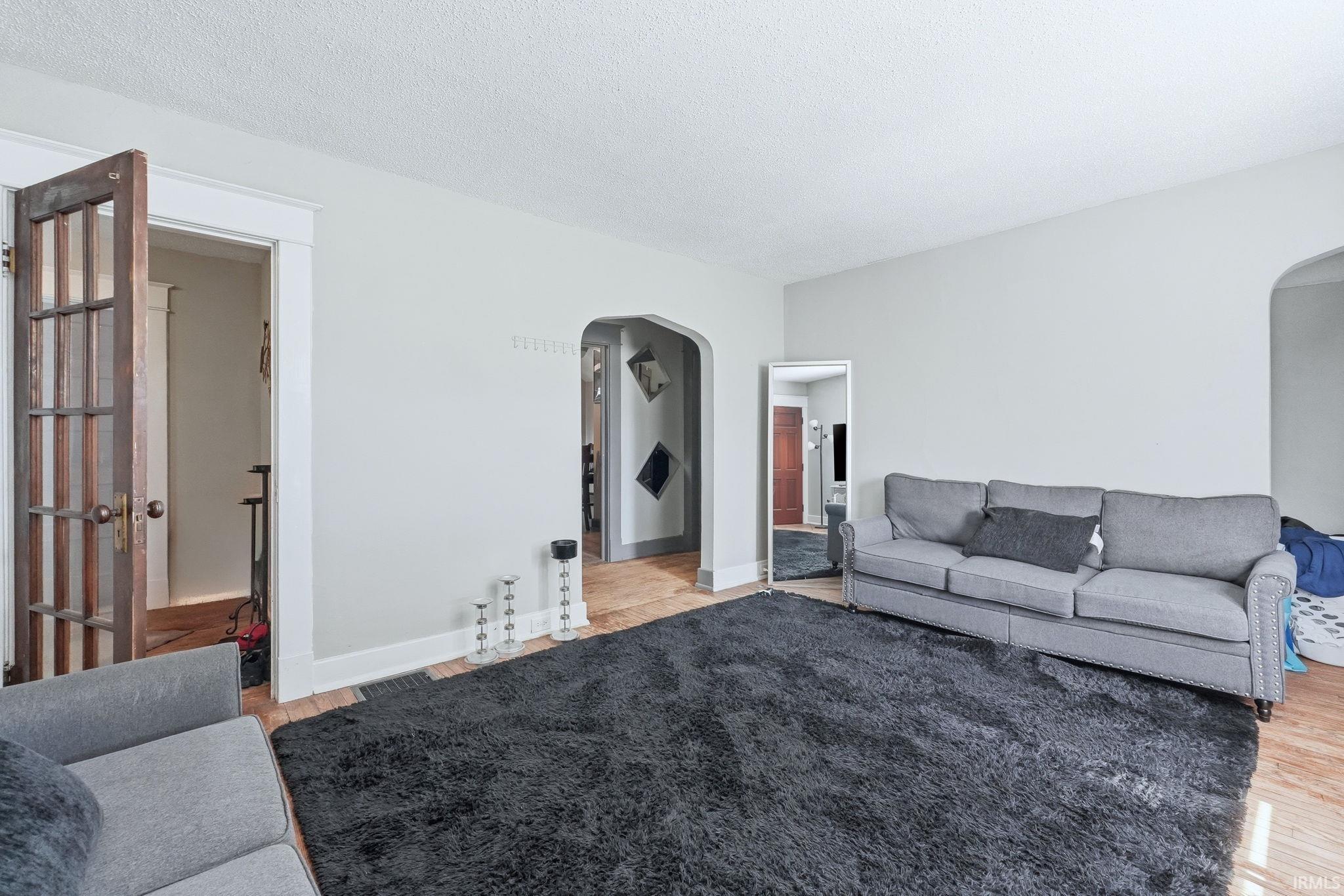 Living area with arched walkways, light wood-type flooring, and a textured ceiling