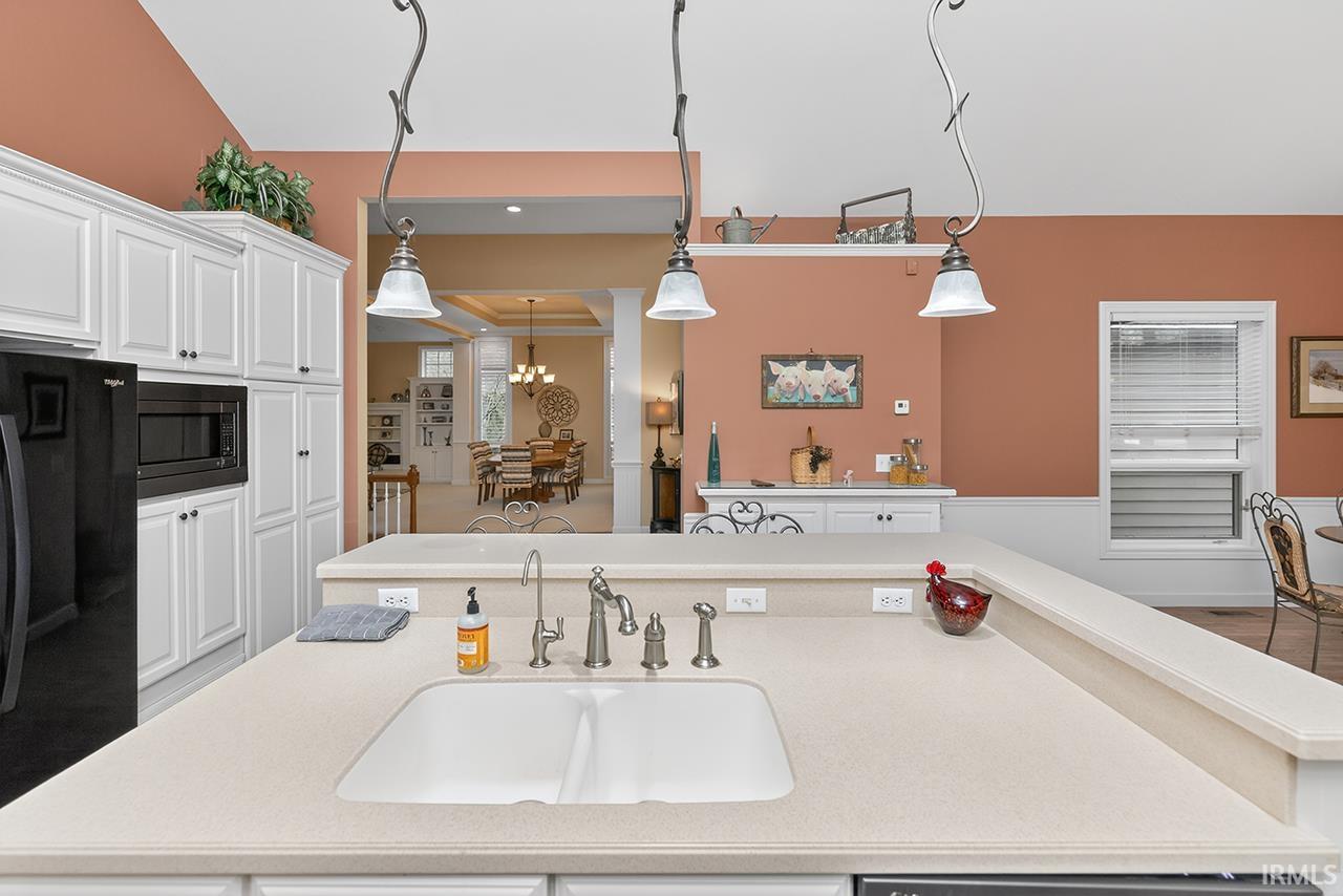 Kitchen featuring white cabinetry, black appliances, hanging light fixtures, and a kitchen island with sink
