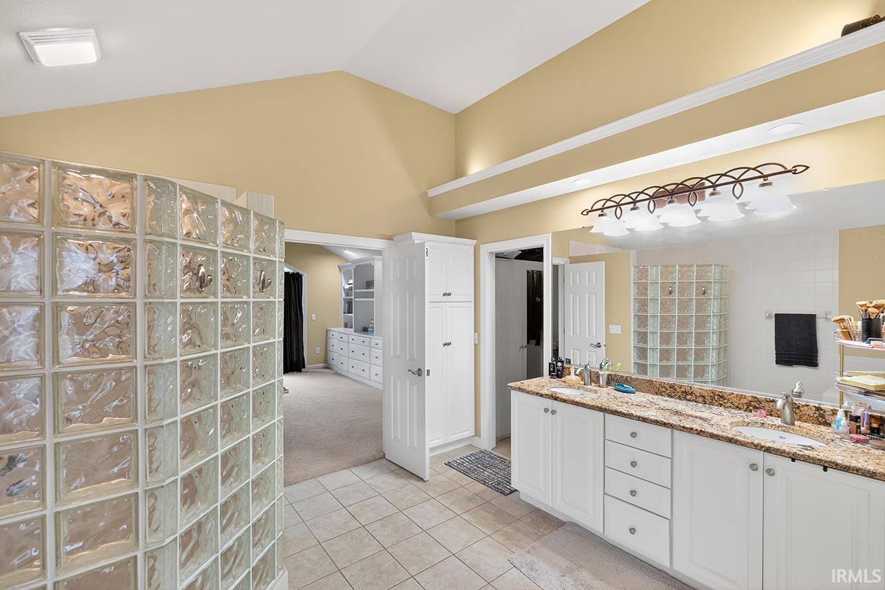 Full bath featuring light carpet, double vanity, light tile patterned floors, and vaulted ceiling