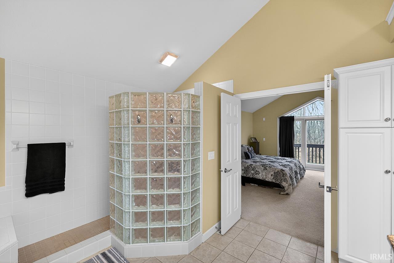Ensuite bathroom with light tile patterned floors, walk in shower, light carpet, and lofted ceiling