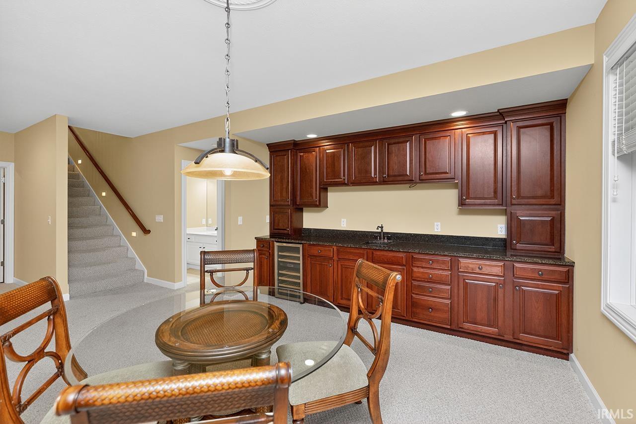 Kitchen with wine cooler, hanging light fixtures, light colored carpet, and dark stone countertops