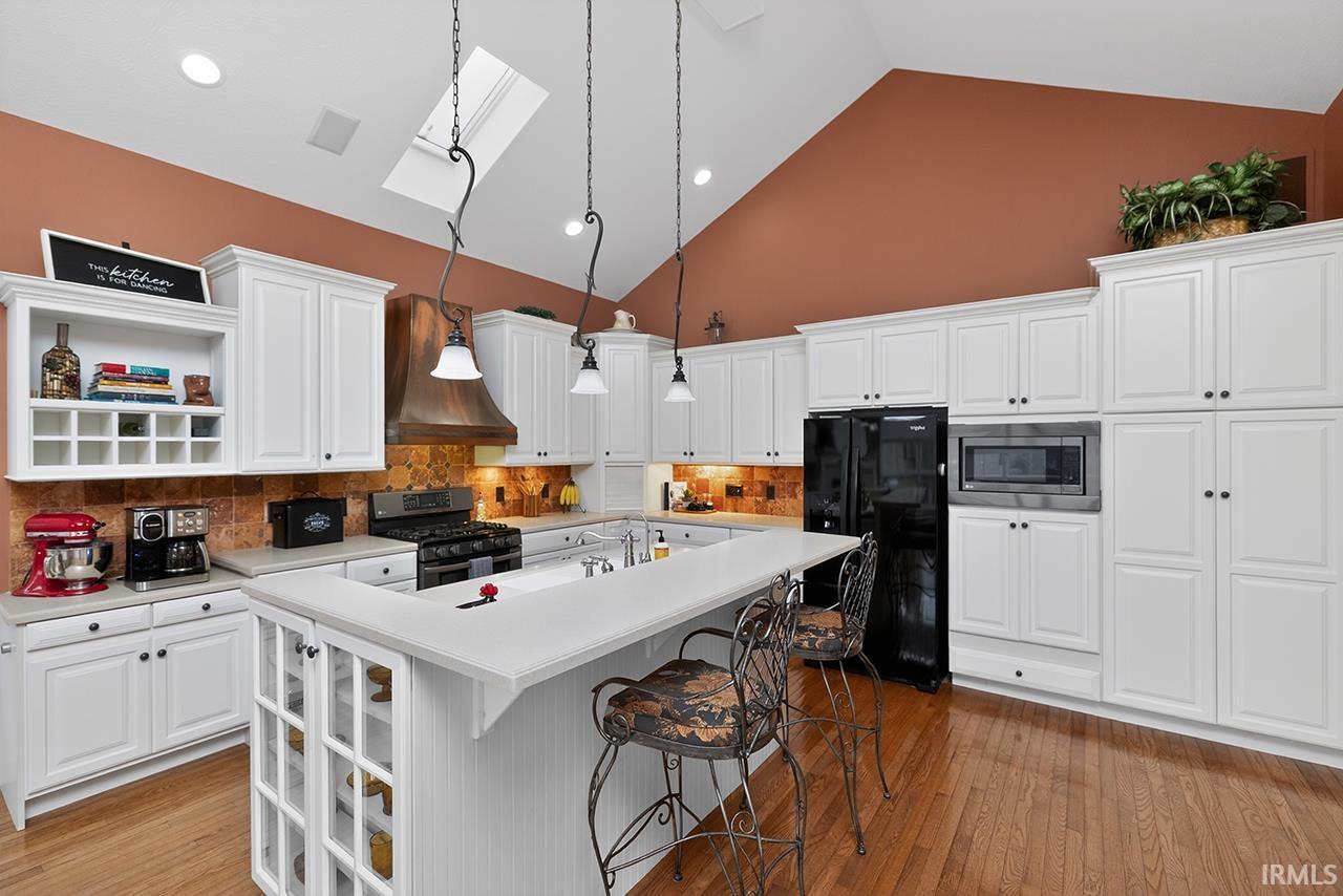 Kitchen with open shelves, a kitchen bar, white cabinets, light countertops, and lofted ceiling