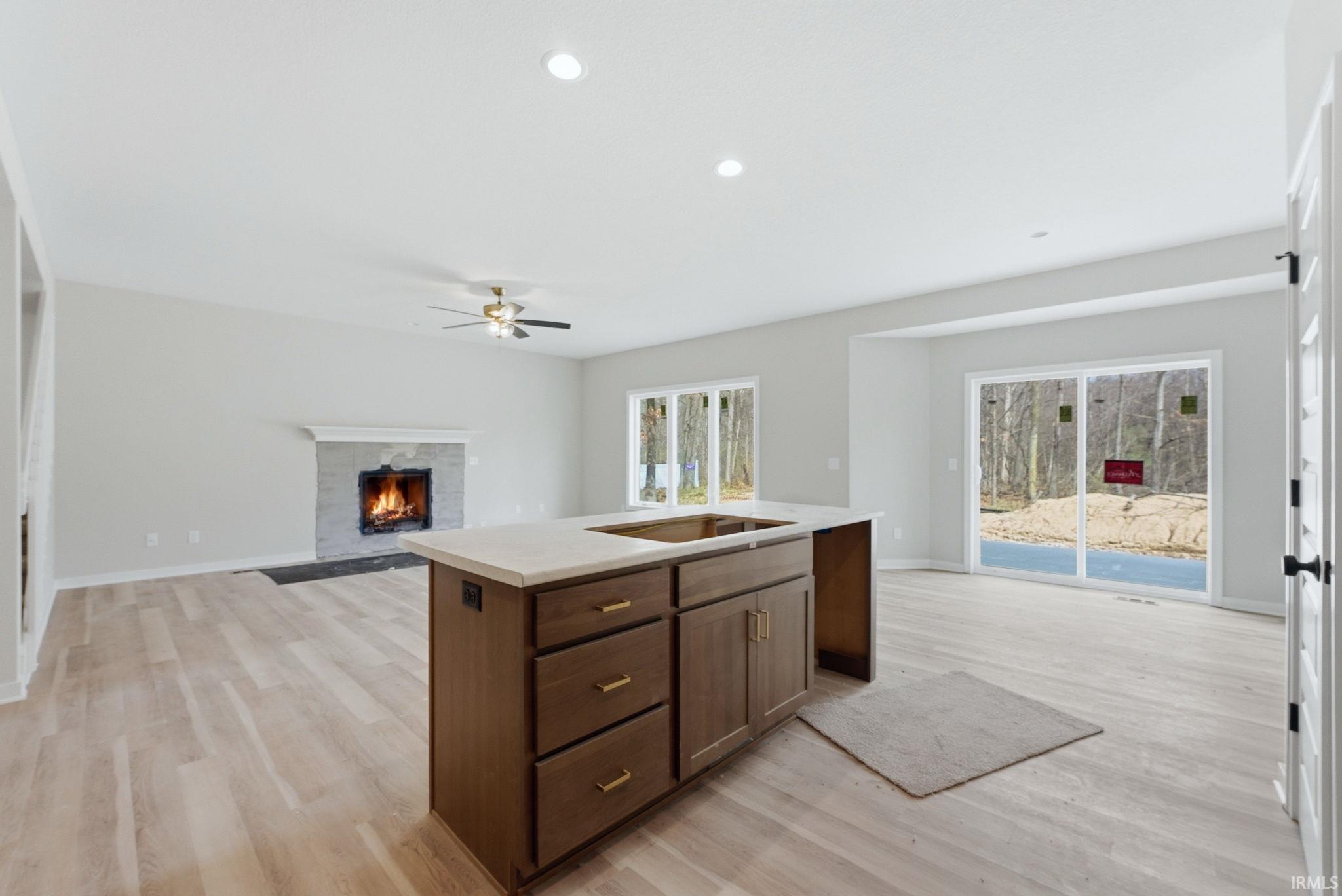 Kitchen featuring open floor plan, a center island with sink, a warm lit fireplace, light wood-style floors, and recessed lighting