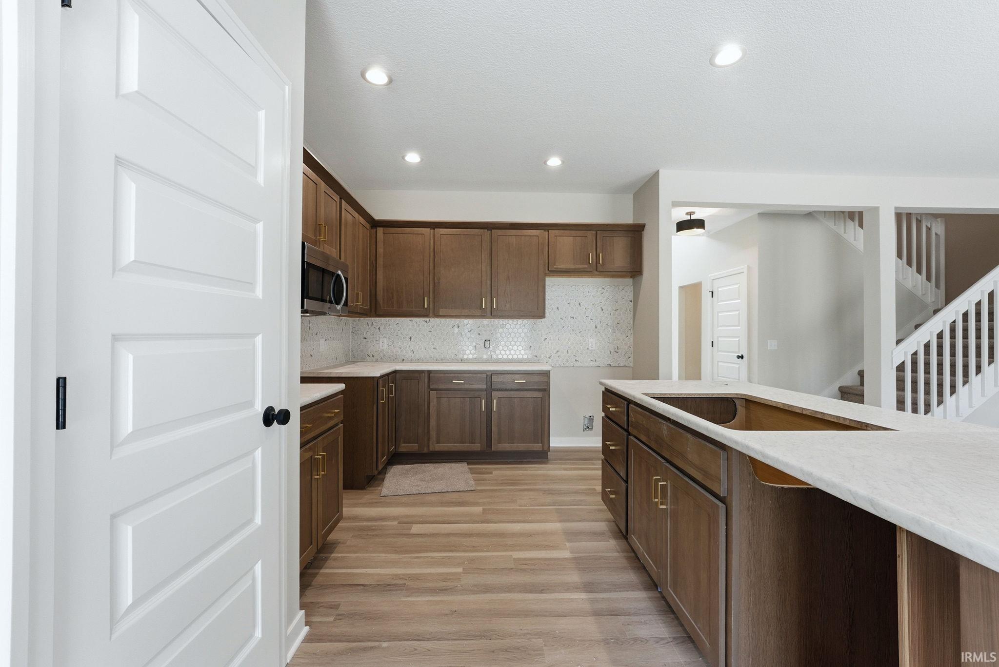 Kitchen with backsplash, light wood-type flooring, stainless steel microwave, recessed lighting, and light stone counters