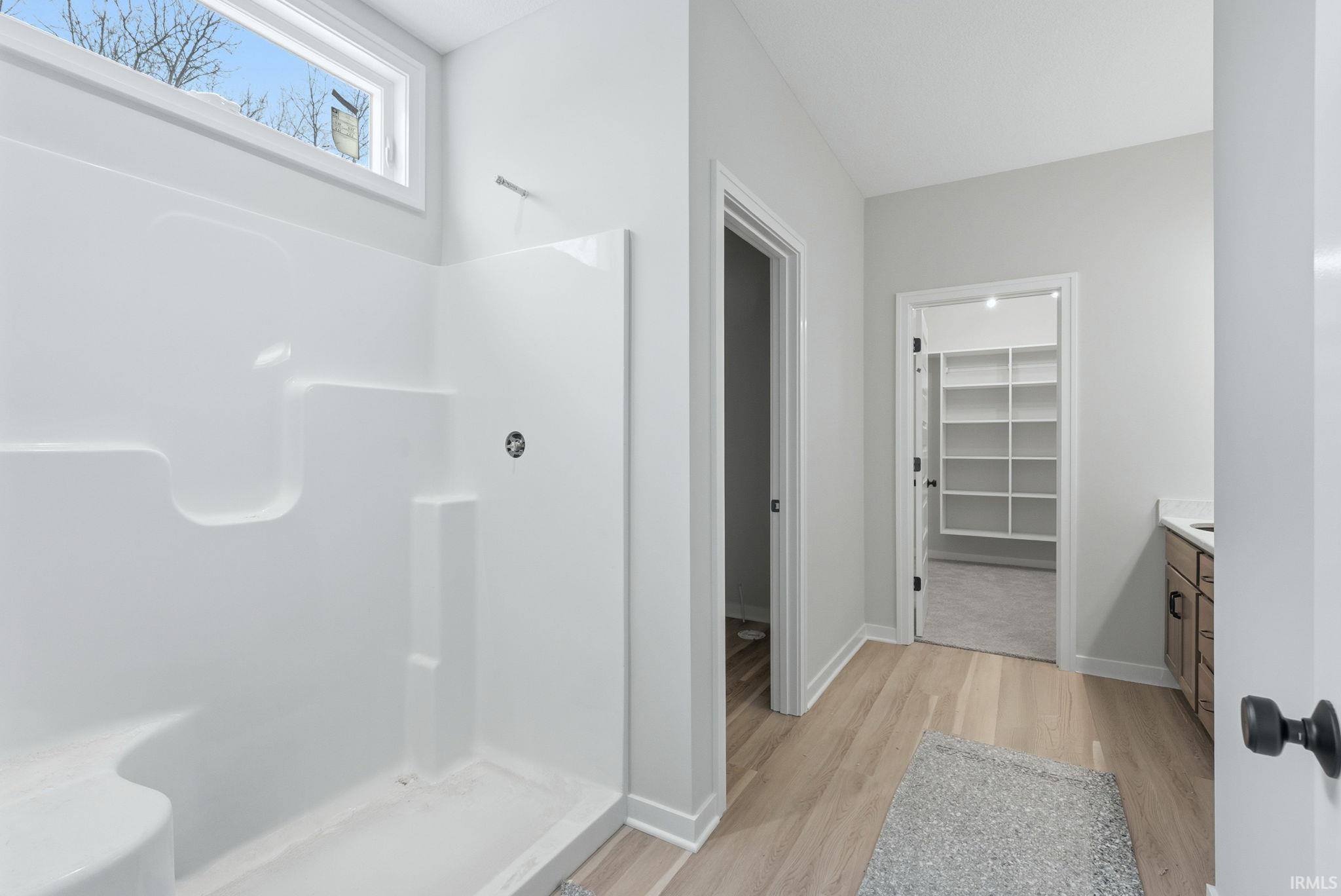 Bathroom featuring a spacious closet, vanity, a stall shower, and light wood-style floors