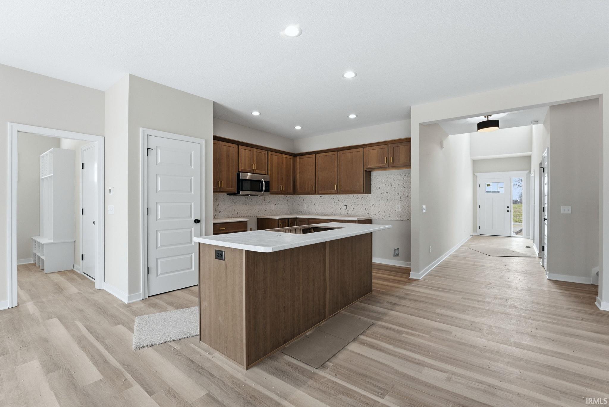Kitchen featuring a kitchen island with sink, light wood finished floors, recessed lighting, wood finish cabinetry, and stainless steel microwave