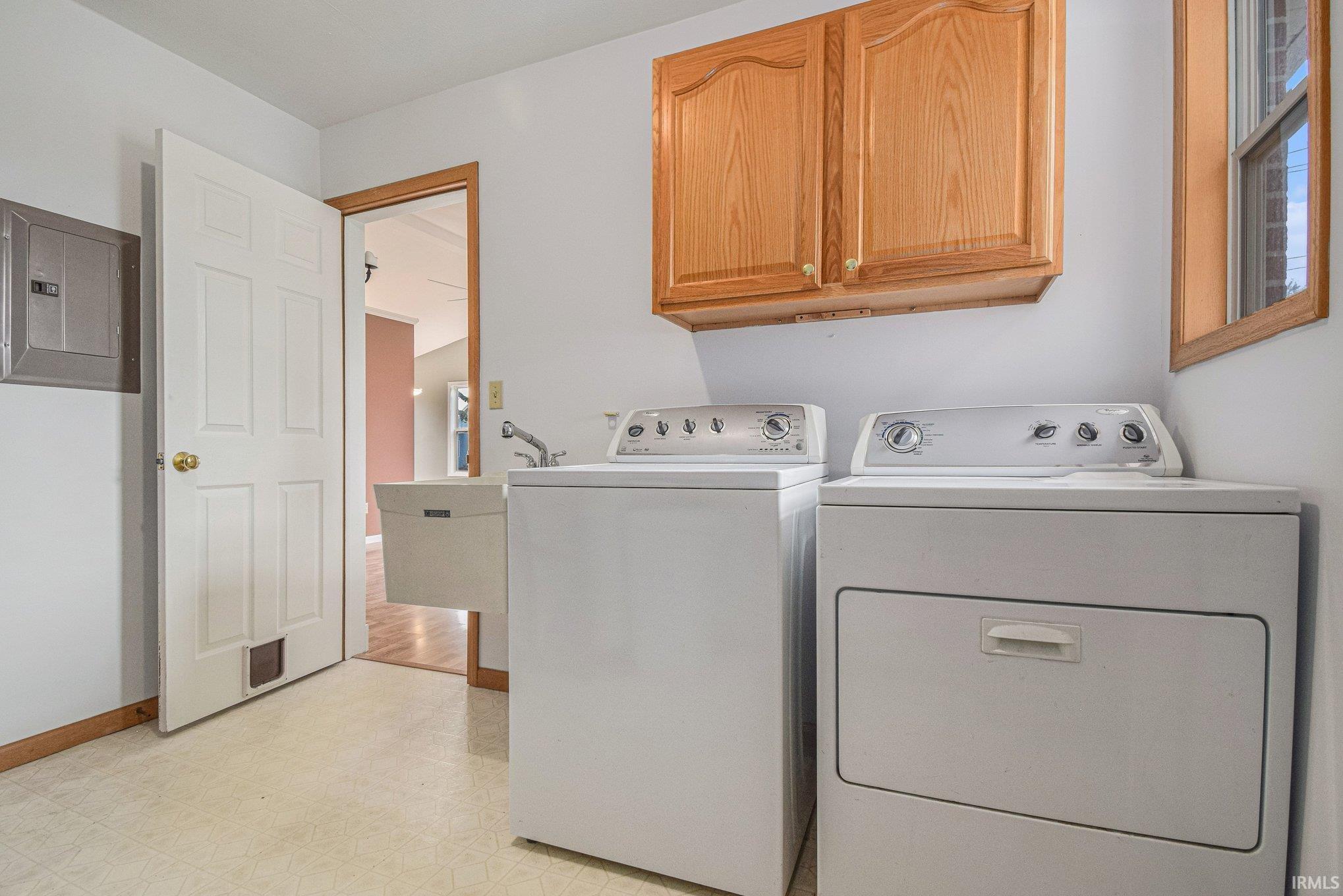 Laundry area featuring light floors, electric panel, cabinet space, and independent washer and dryer