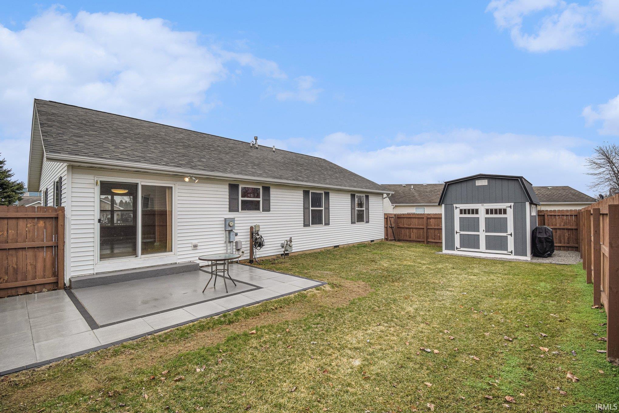 Rear view of property with a fenced backyard, a storage unit, a patio area, and a shingled roof