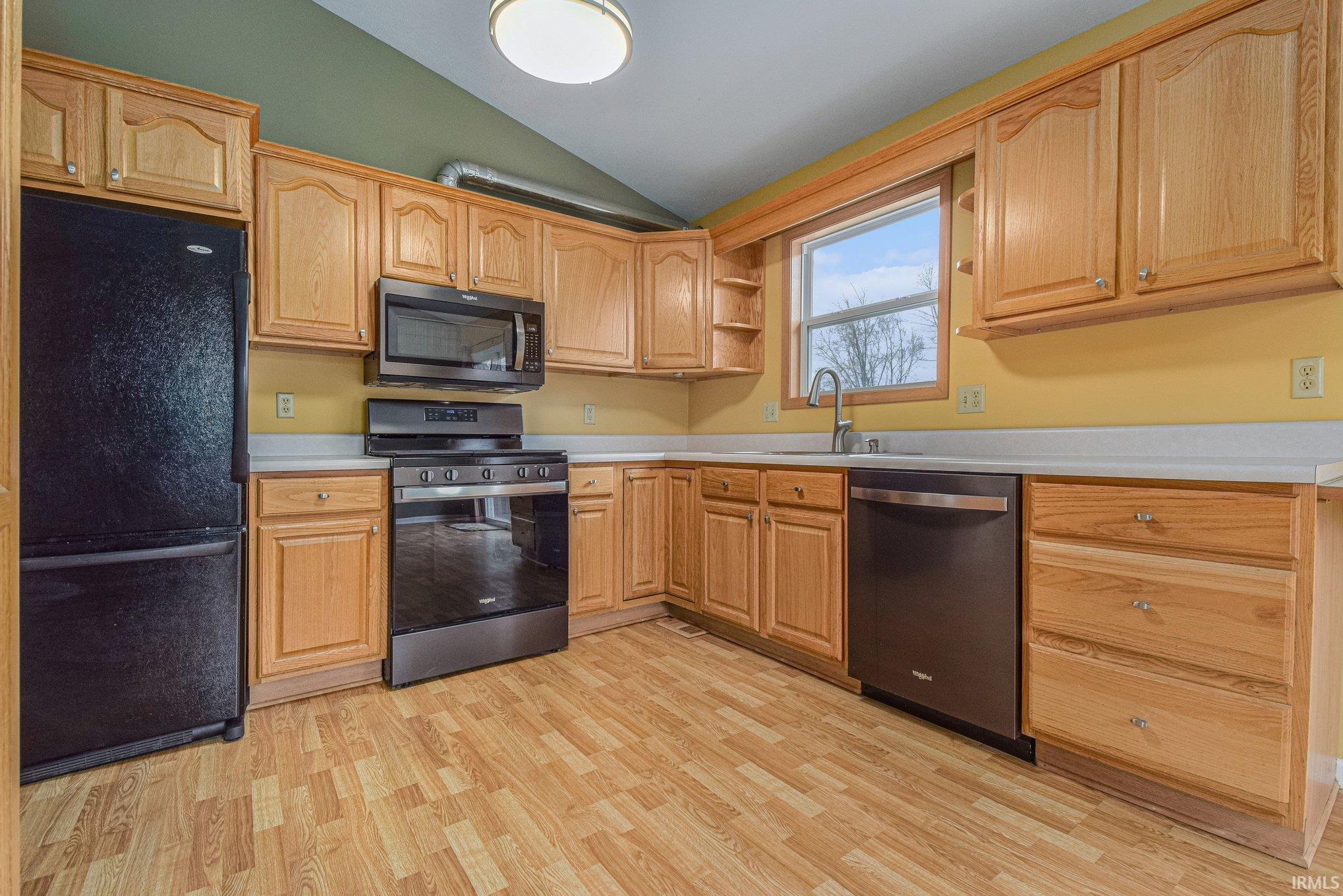 Kitchen with stainless steel appliances, lofted ceiling, light countertops, light wood finished floors, and open shelves