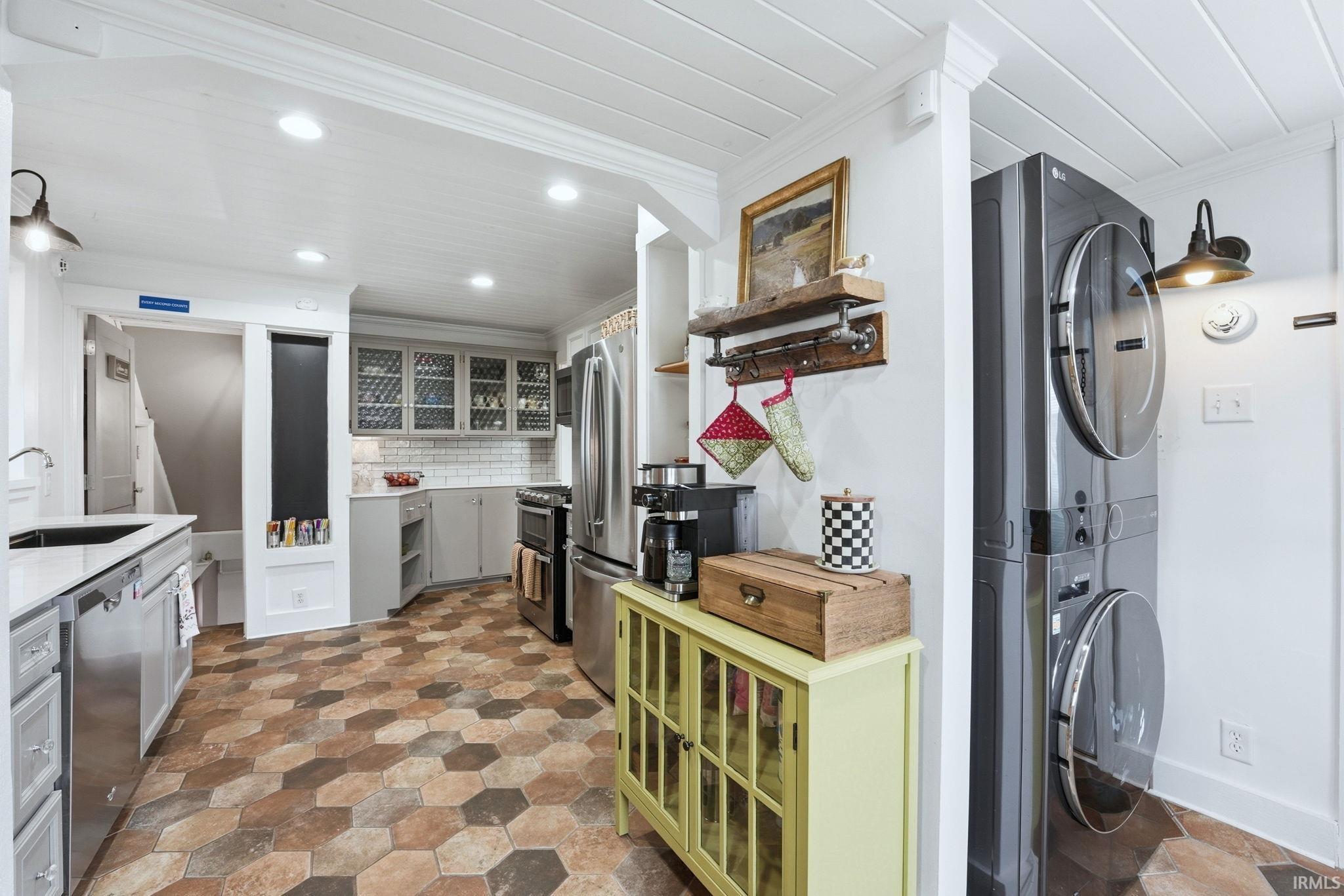 Kitchen featuring gray cabinets, ornamental molding, stainless steel appliances, decorative backsplash, and stacked washer / drying machine