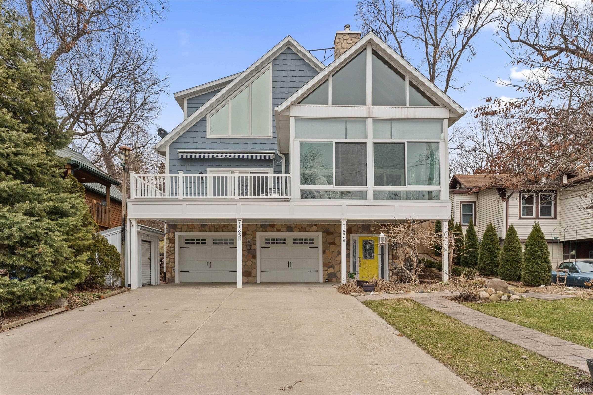 View of front of house with concrete driveway, an attached garage, a chimney, stone siding, and a deck