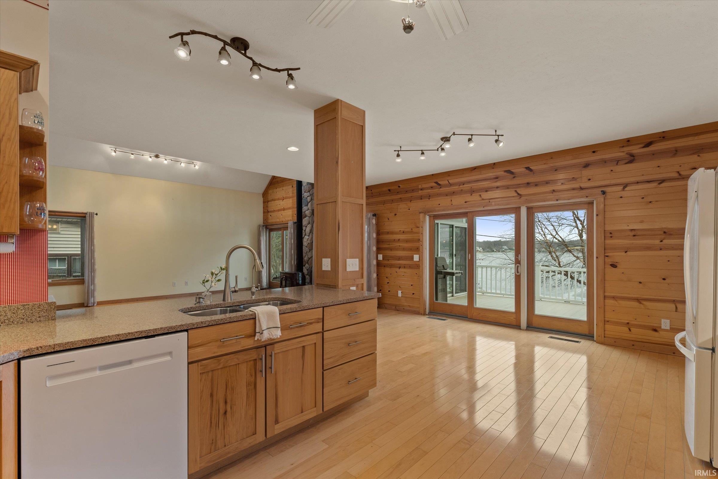 Kitchen featuring white appliances, light stone countertops, wooden walls, a peninsula, and plenty of natural light