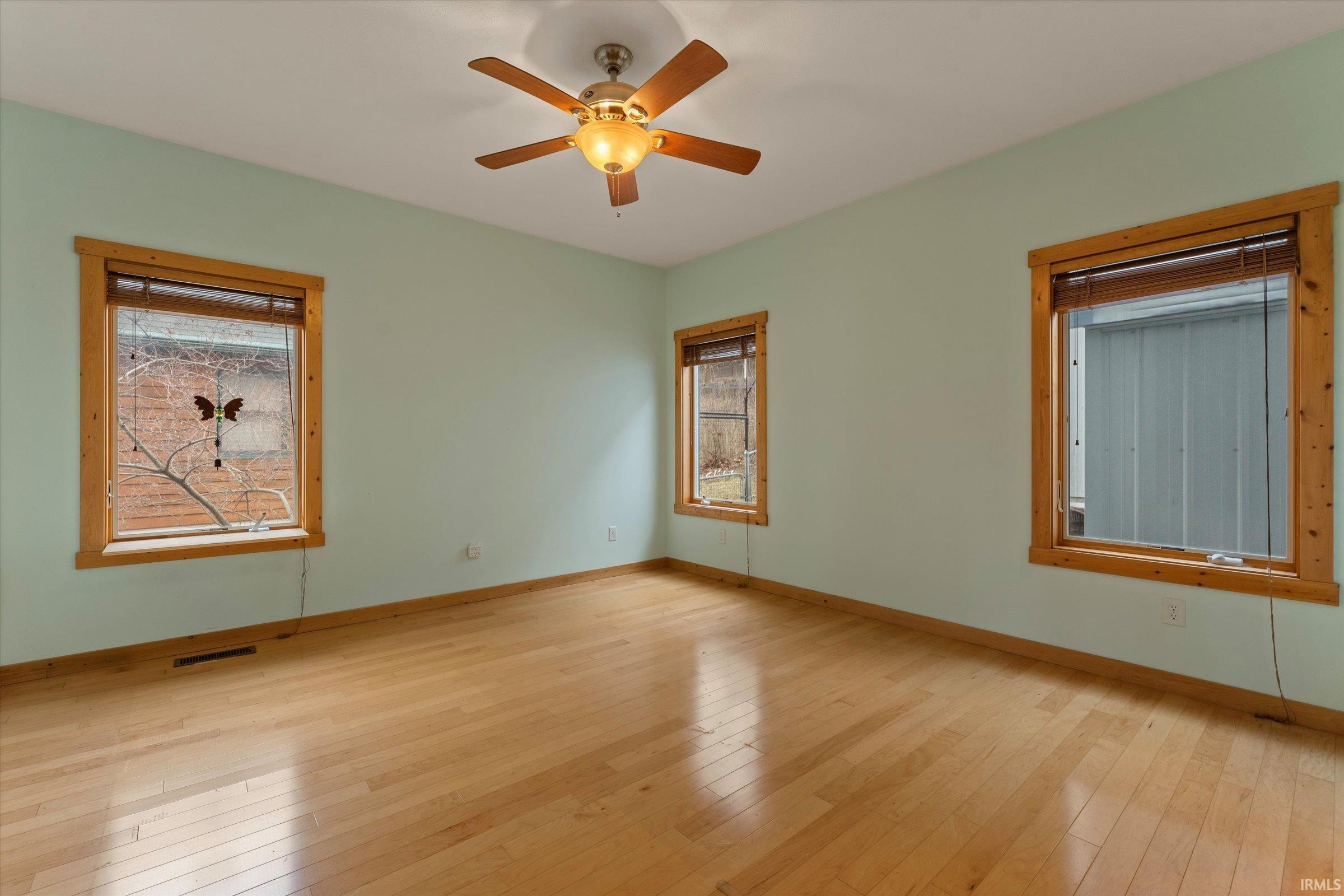 Empty room featuring light wood finished floors, healthy amount of natural light, and ceiling fan