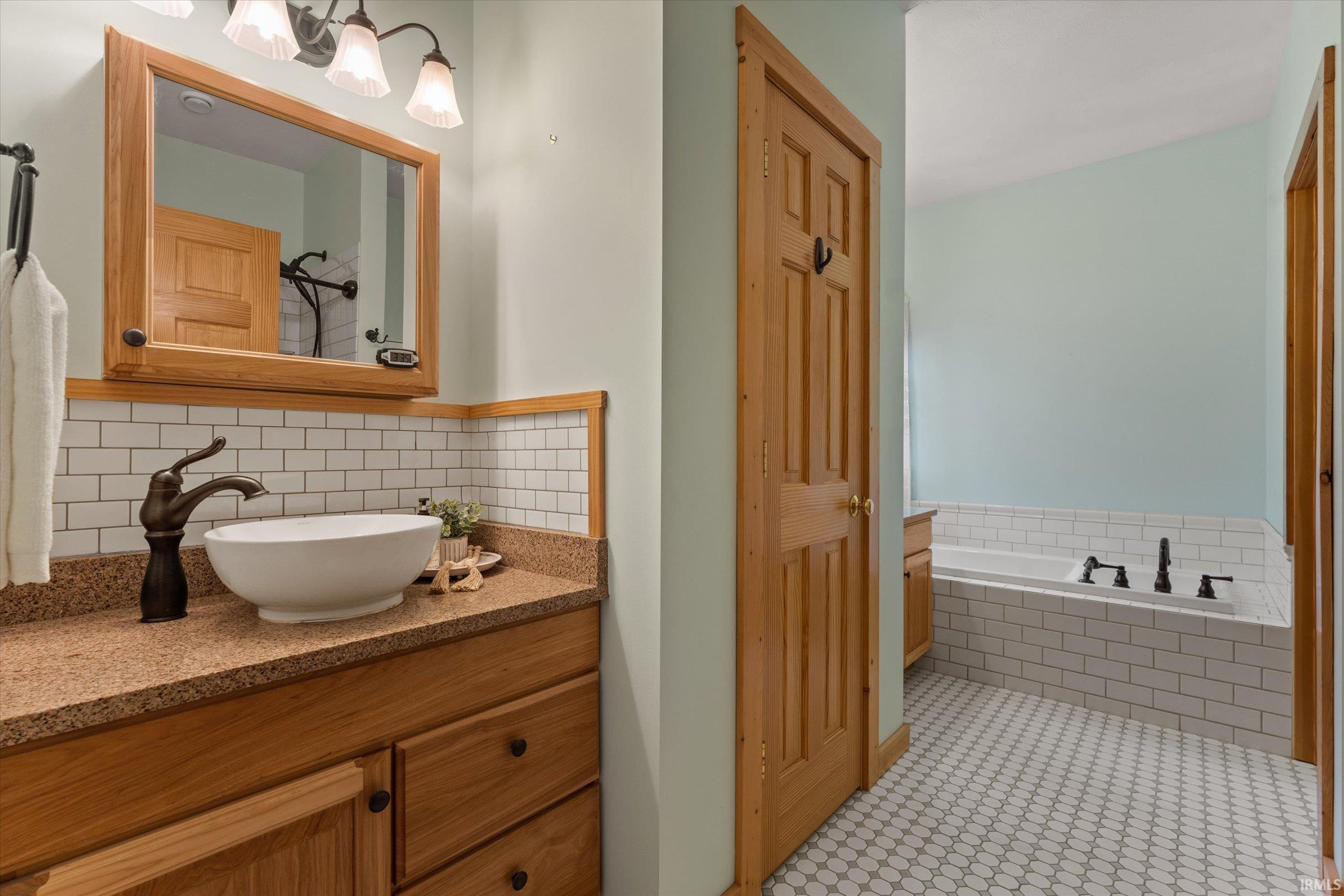Bathroom featuring a bath, vanity, and decorative backsplash