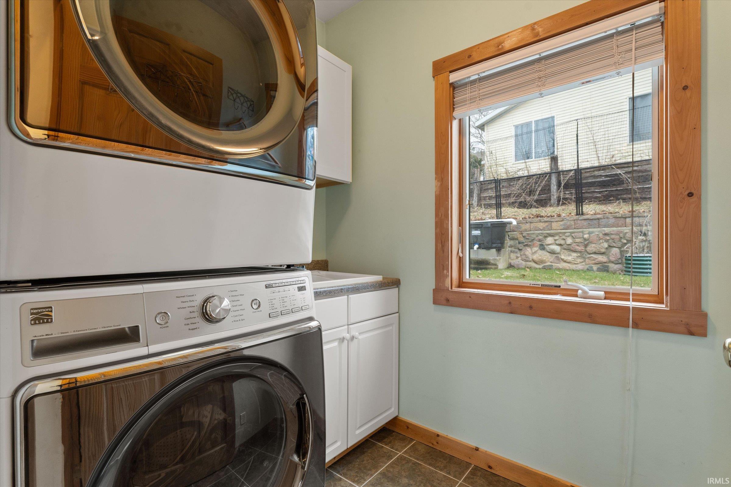 Laundry area featuring stacked washer and dryer, cabinet space, and dark tile patterned flooring