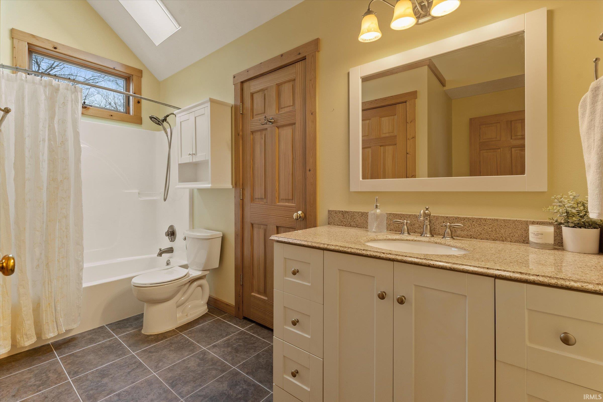 Full bath with vanity, vaulted ceiling, shower / bath combo, a skylight, and dark tile patterned flooring